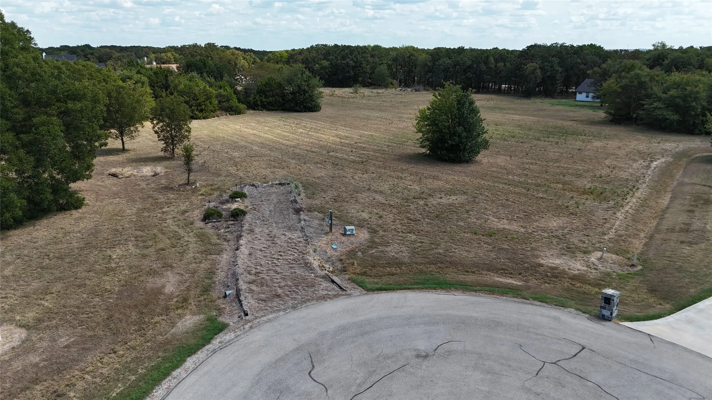 Expansive cleared parcel featuring mature trees, established landscaping, and paved street access