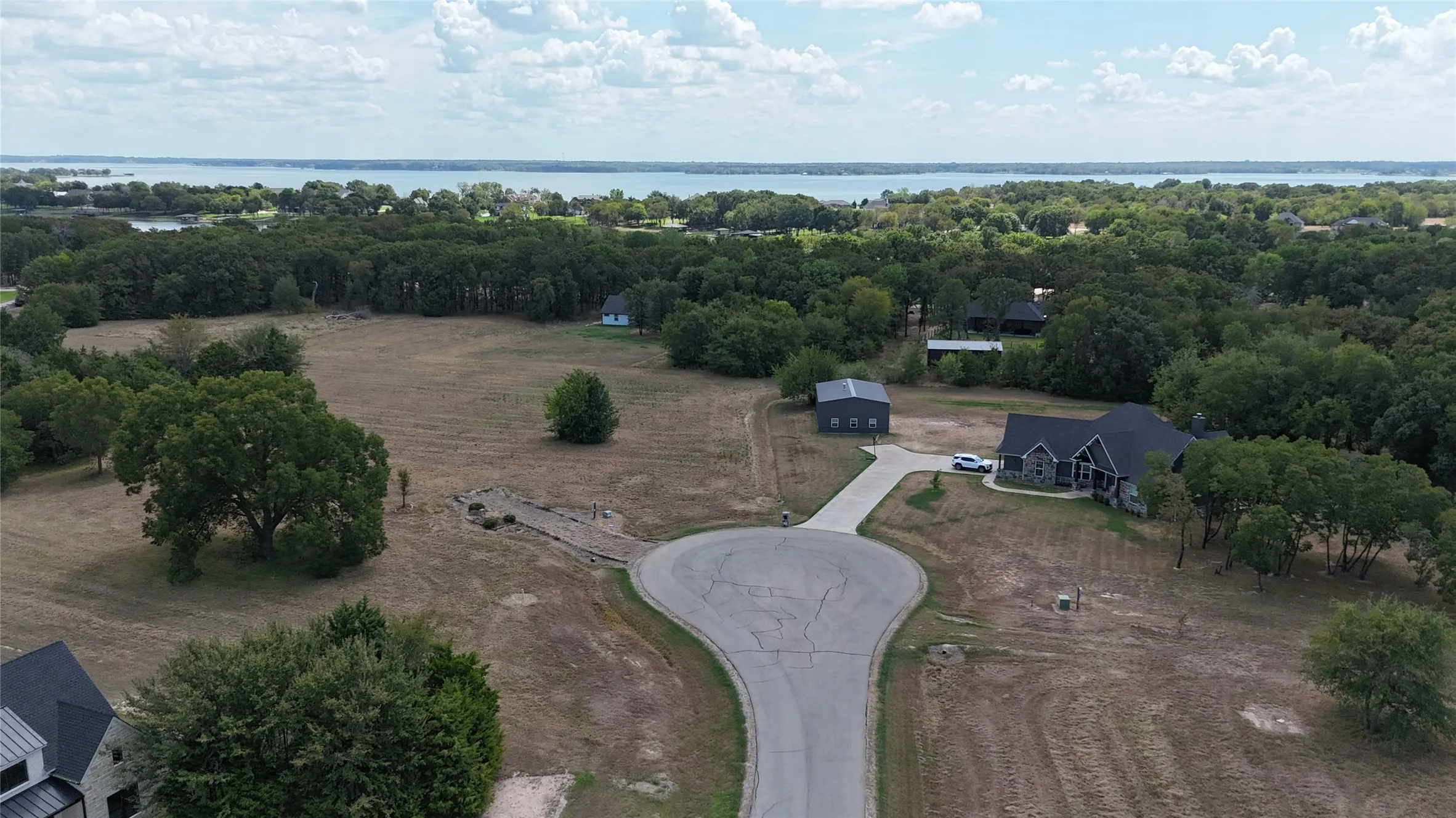 Expansive acreage featuring a residential structure, a detached outbuilding, a concrete driveway, and mature tree clusters