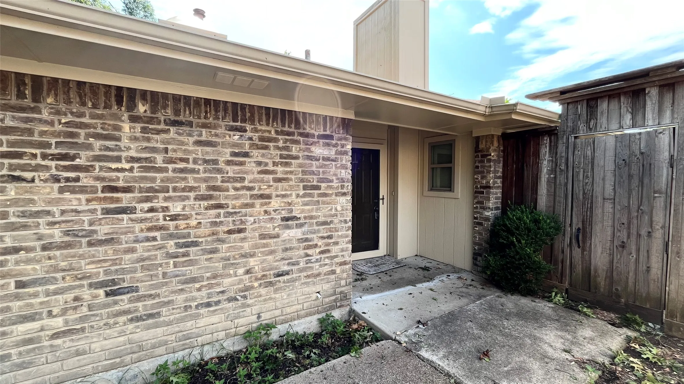Exterior featuring a multi-toned brick facade, vertical wood-panel siding, a covered entryway, and a solid-panel front door