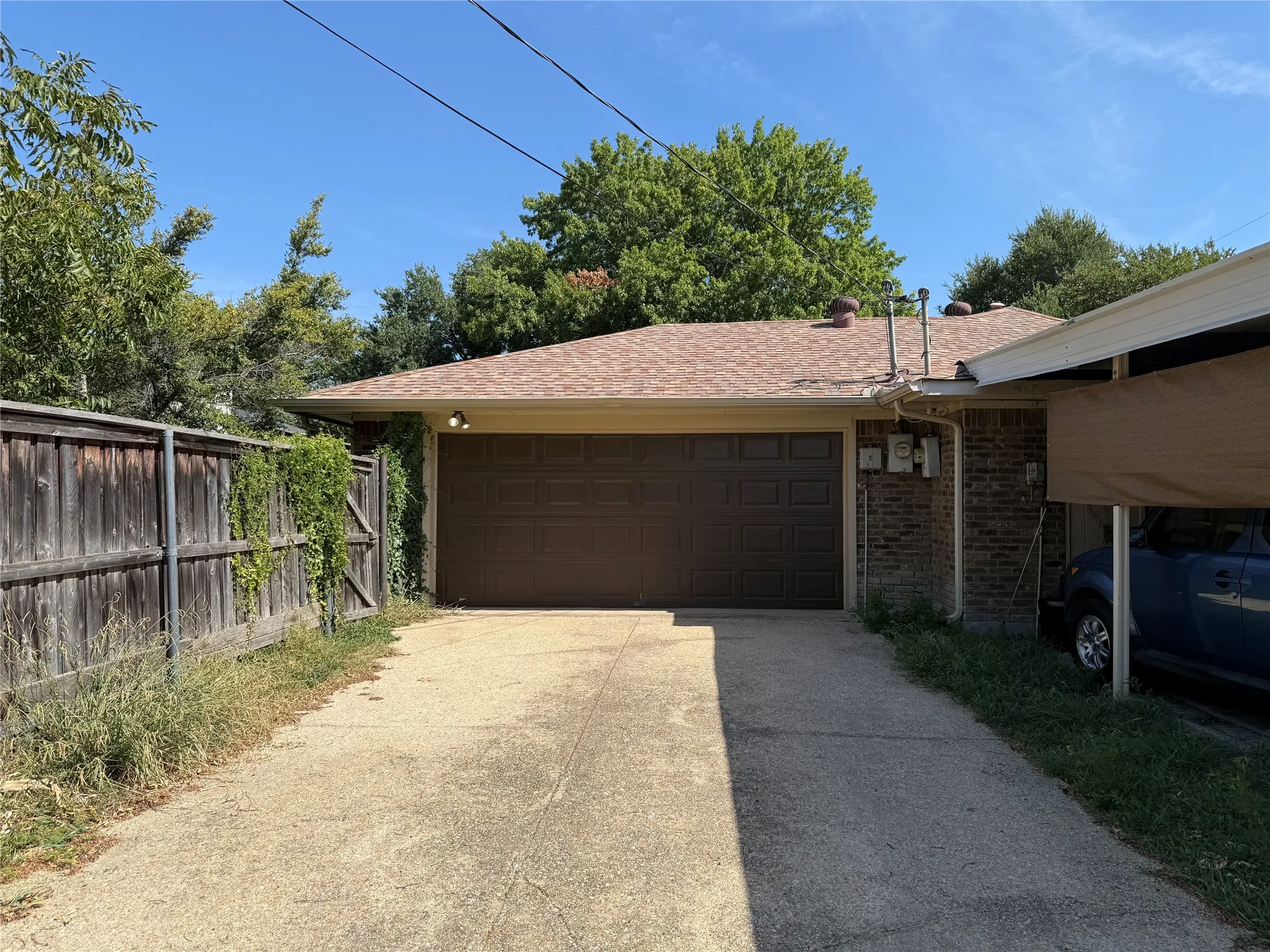 Detached two-car garage with sectional door, masonry exterior, asphalt shingle roof, and attached carport