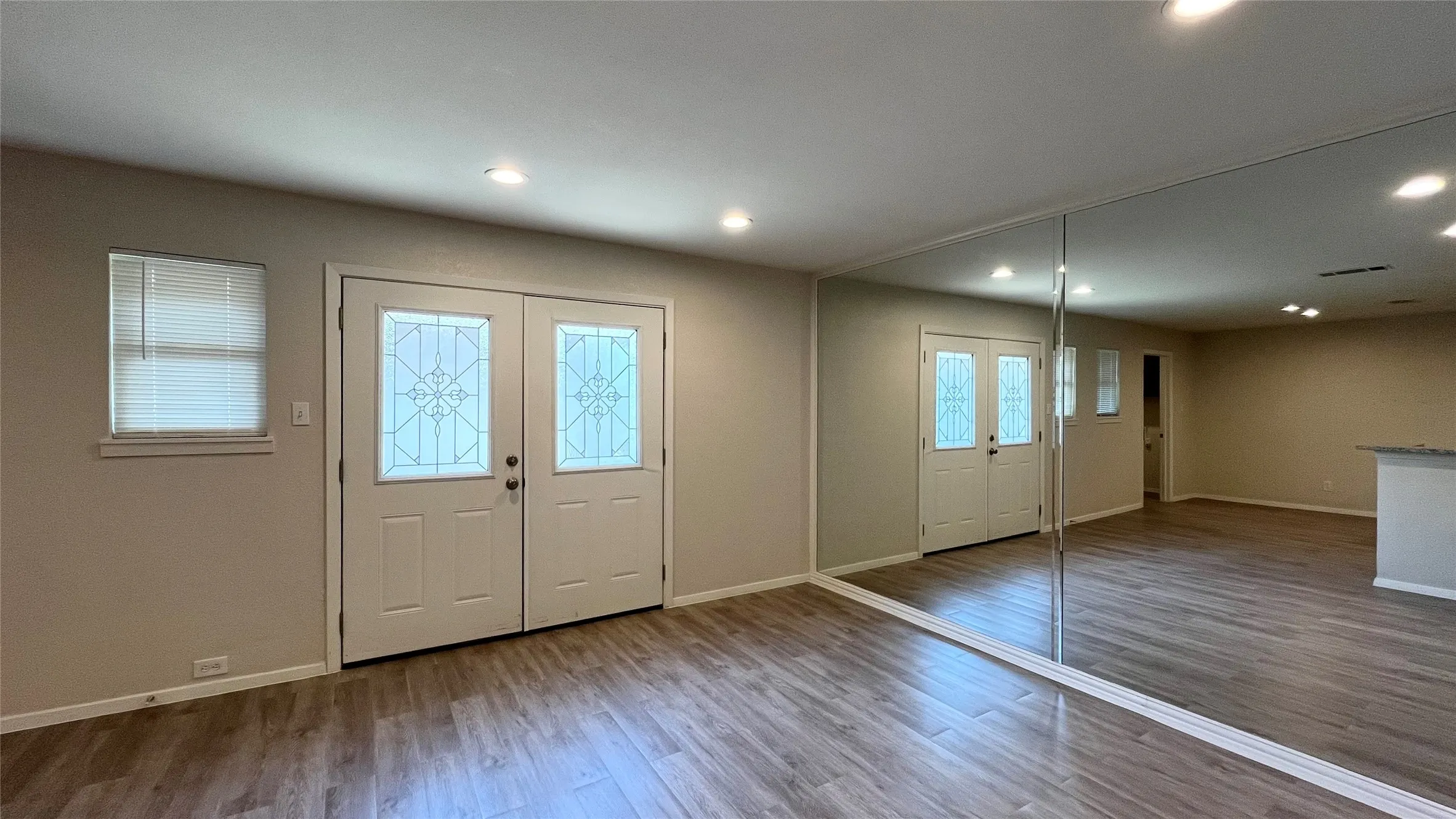 Double entry doors with decorative glass inserts, recessed lighting, wood-finish flooring, and a floor-to-ceiling mirrored wall
