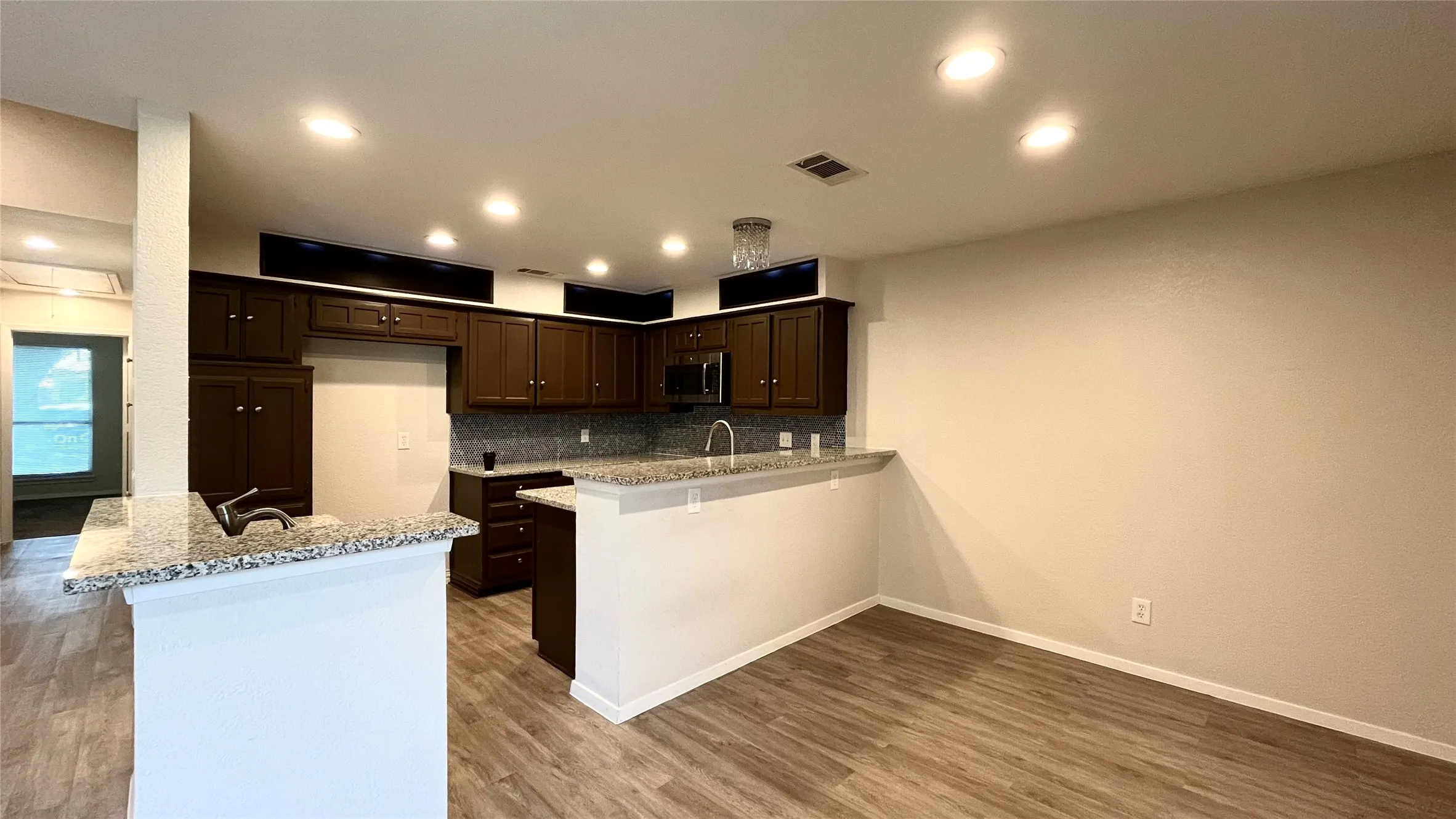 Kitchen featuring dark cabinetry, stone-surface countertops, wood-finish flooring, recessed lighting, and a breakfast bar