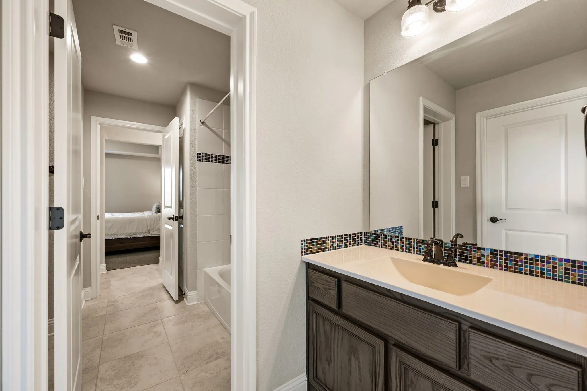 Vanity featuring stained wood-finish cabinetry, a solid-surface countertop with an integrated sink, multi-colored glass tile backsplash, and a large wall-mounted mirror