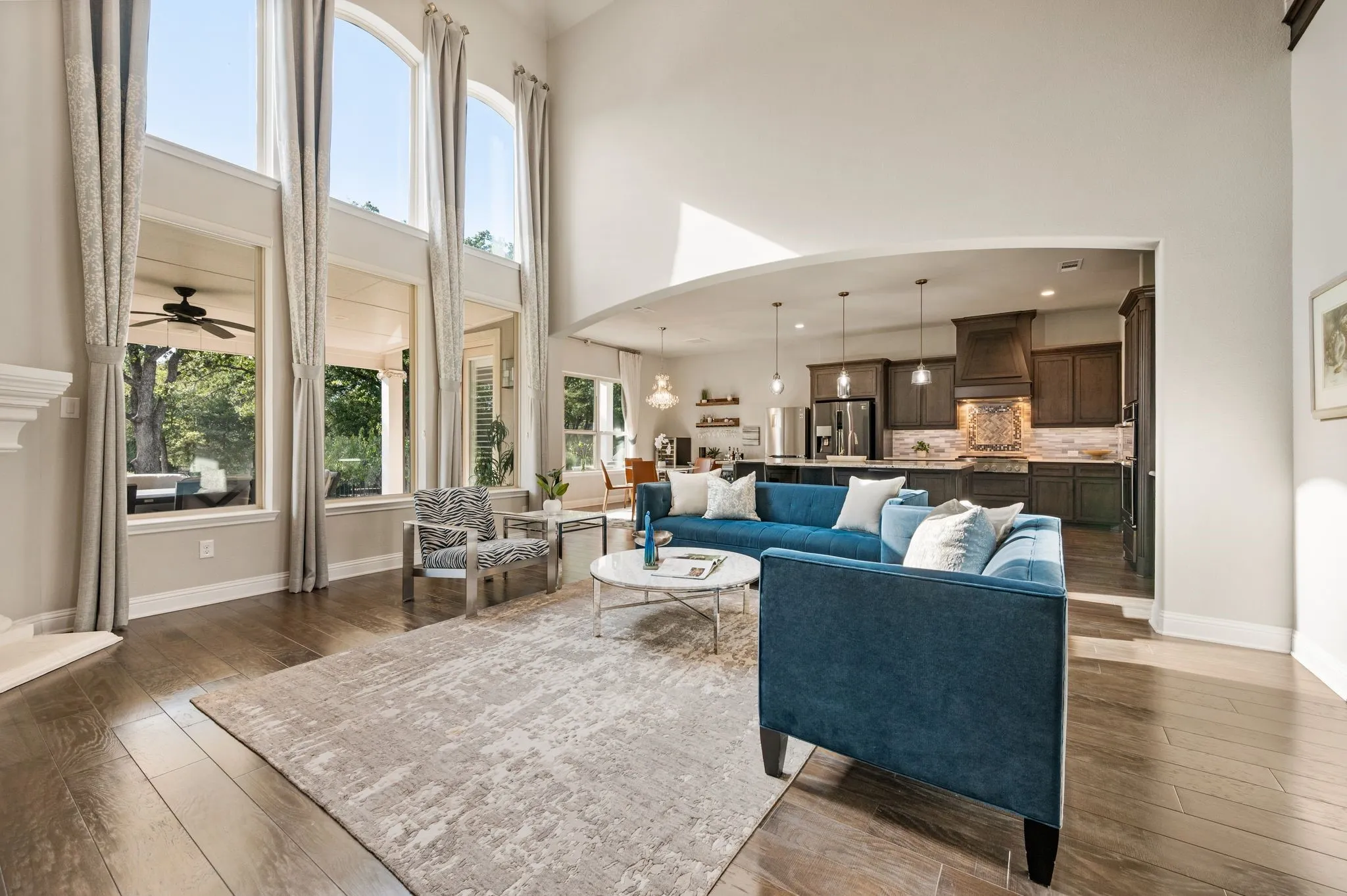 Expansive living area featuring vaulted ceilings, floor-to-ceiling arched windows, wood-finish flooring, and open-concept design with built-in kitchen cabinetry
