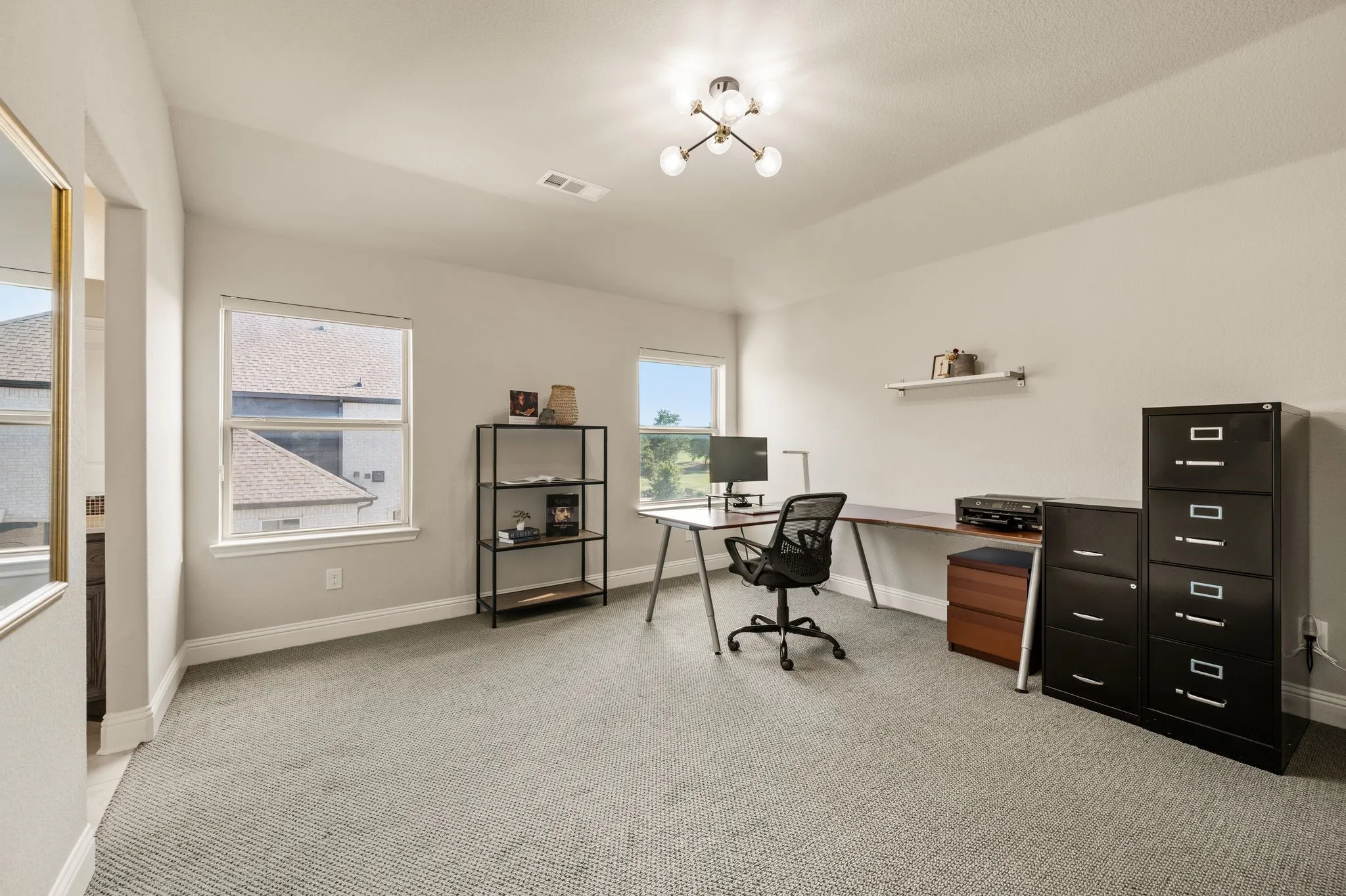 Neutral-toned bedroom featuring textured carpeting, multiple windows, a ceiling-mounted multi-arm light fixture, and a wall-mounted display shelf