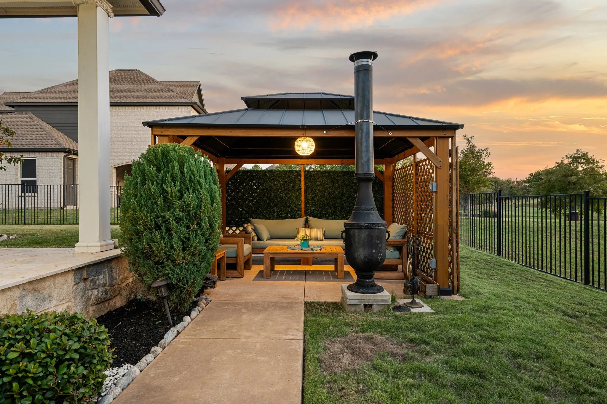 Outdoor living area featuring a wood-frame gazebo with a metal roof, concrete patio flooring, privacy lattice, and a tall metal chiminea