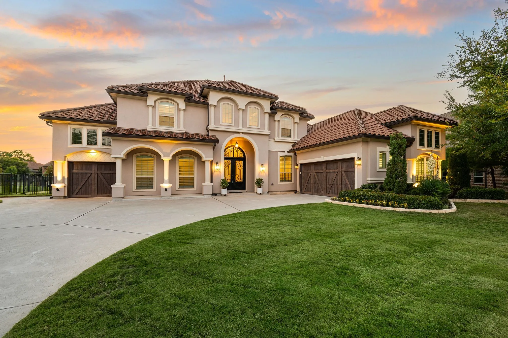 Mediterranean-style home featuring a tile roof, arched entryway, 3 car garage with wood-finish doors, stucco facade, and professional landscaping
