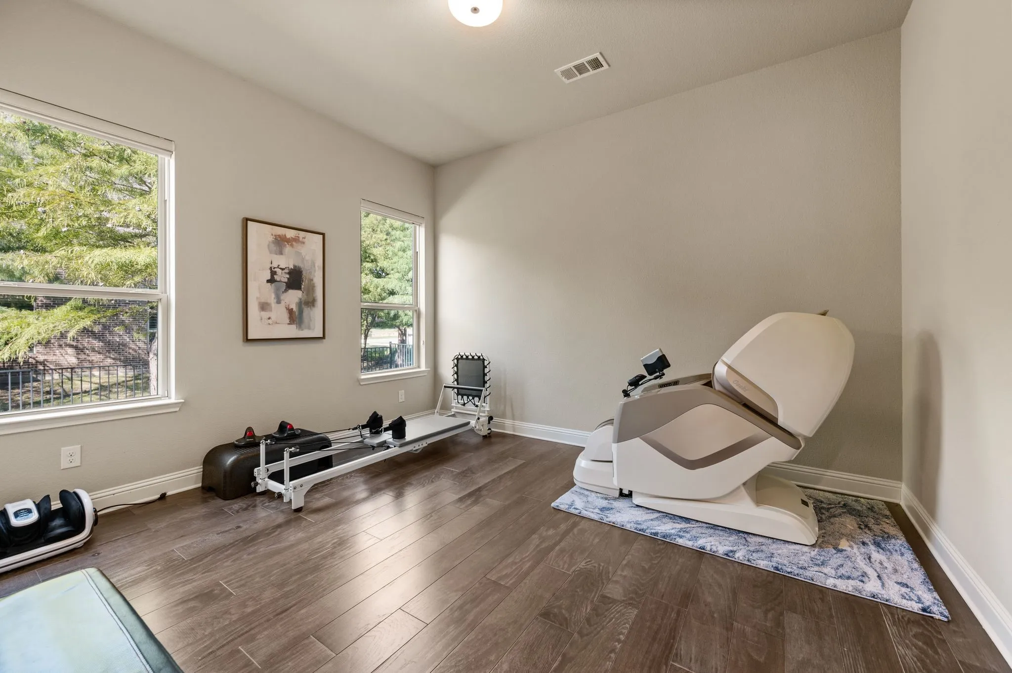 Downstairs guest bedroom featuring wood-finish flooring, neutral wall paint, and two large windows with natural light exposure