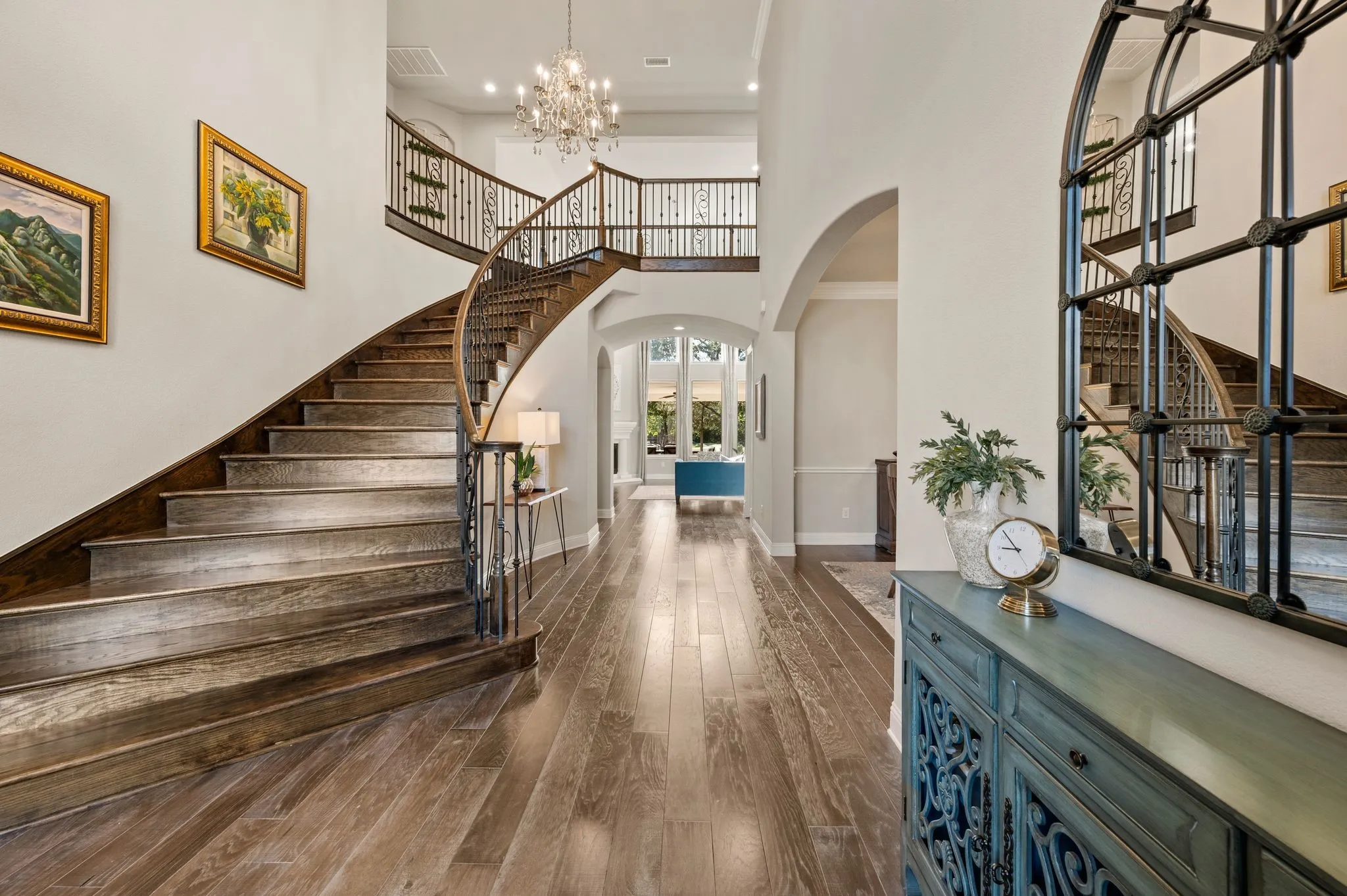 Curved staircase featuring wood-finish treads, a decorative metal balustrade, and a stained wood handrail, complemented by wood-finish flooring, recessed lighting, and a multi-tiered crystal chandelier
