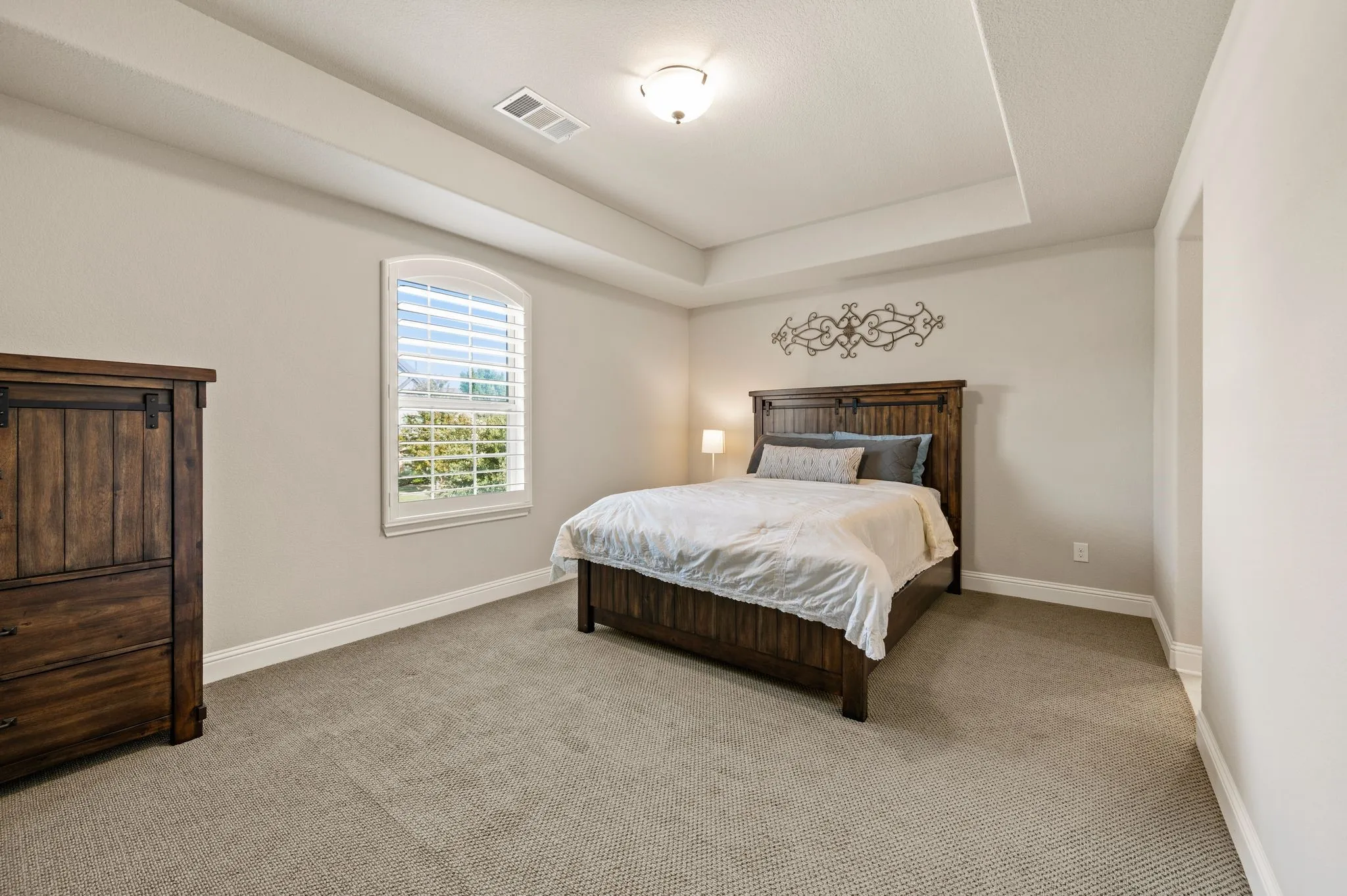 Tray ceiling, neutral wall tones, arched window with plantation shutters, and textured wall-to-wall carpeting