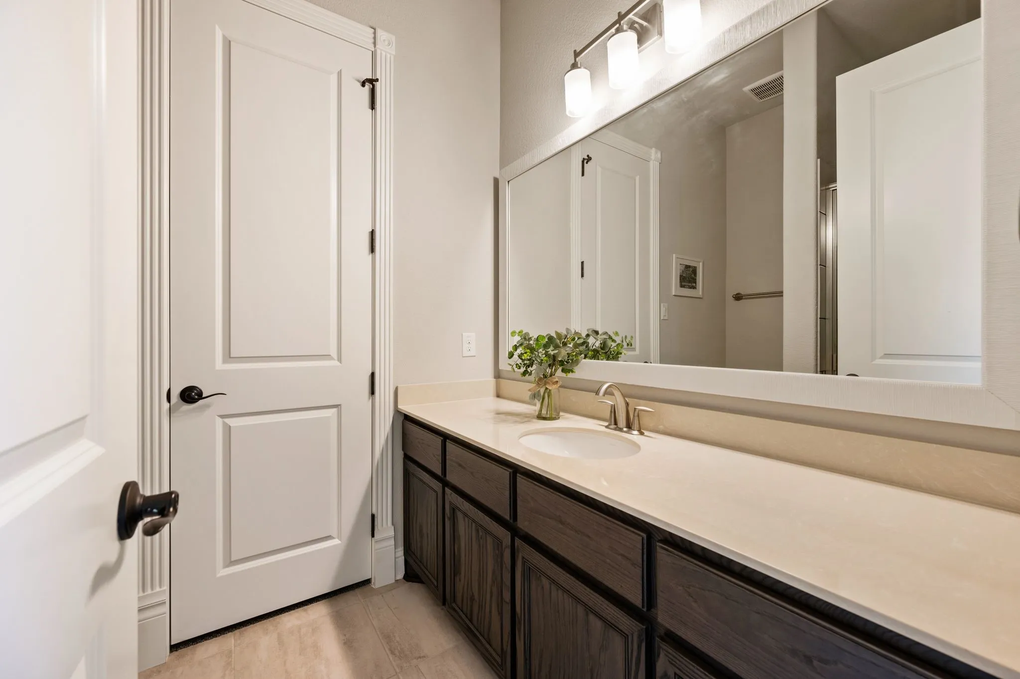 Bathroom vanity featuring dark-stained wood cabinetry, solid-surface countertop with an integrated basin, expansive framed mirror, and a multi-light fixture