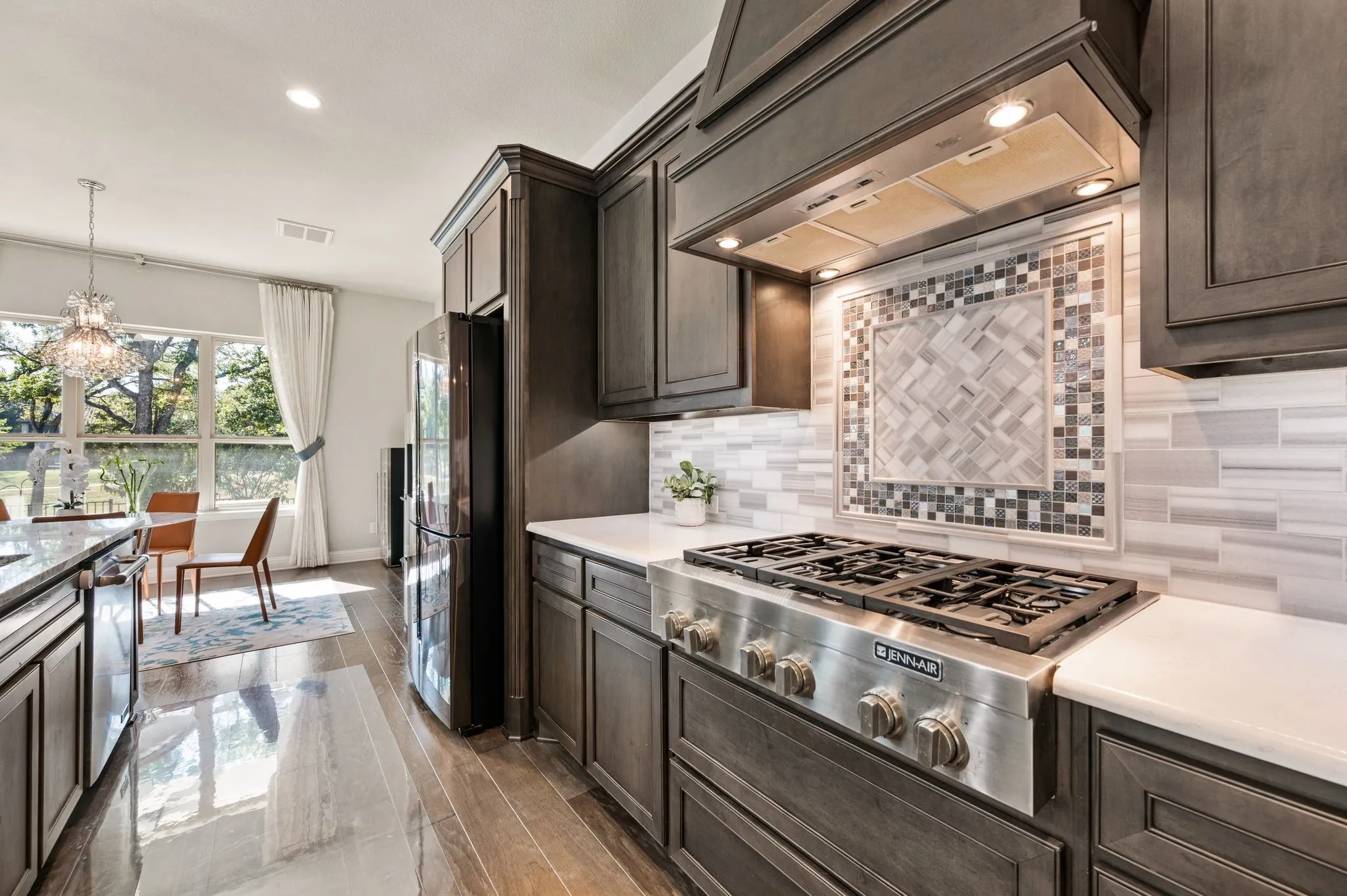 Kitchen featuring dark-stained wood cabinetry, light-toned stone countertops, a professional-grade stainless steel gas range with a matching range hood, and a decorative tile backsplash