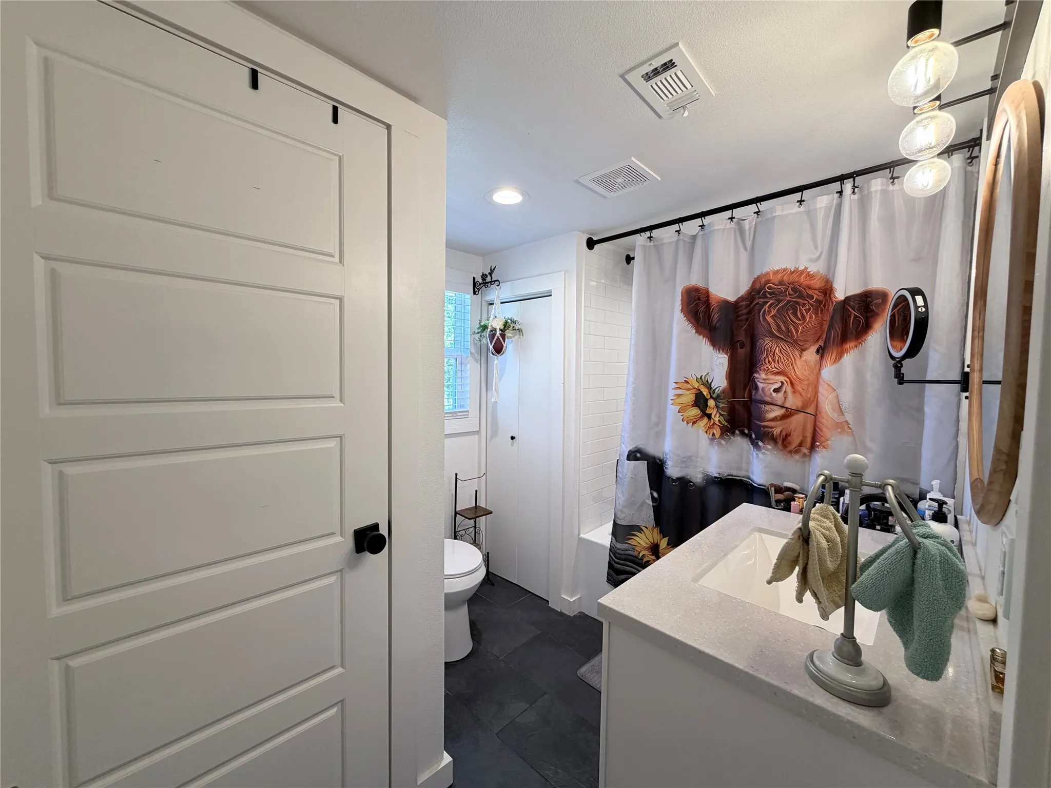 Bathroom featuring a vanity with a light-toned countertop, a tiled tub surround, dark stone-finish flooring, and a multi-panel door with matte black hardware