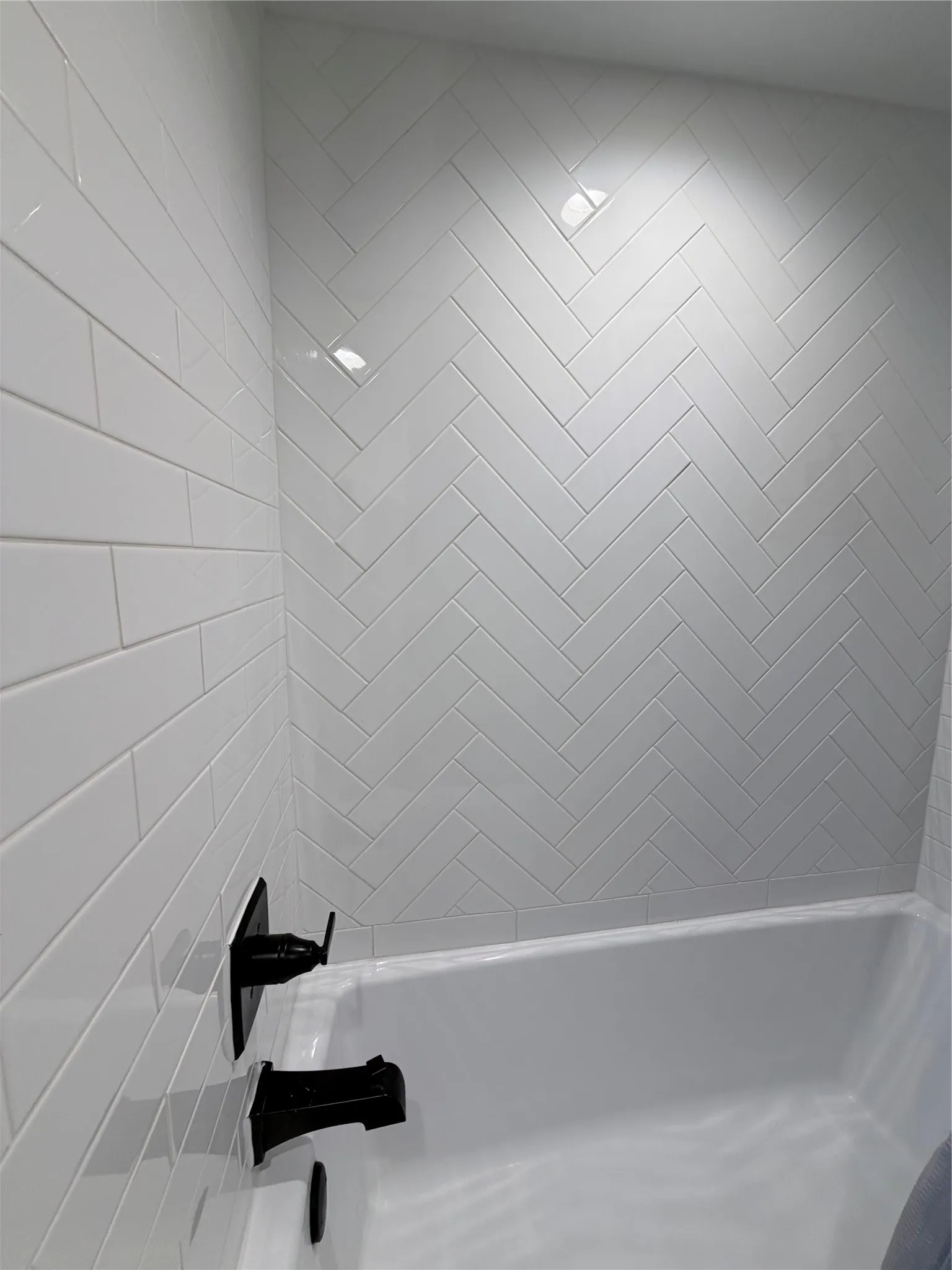 White subway tile surround in a herringbone pattern, paired with matte black wall-mounted plumbing fixtures and a deep soaking tub