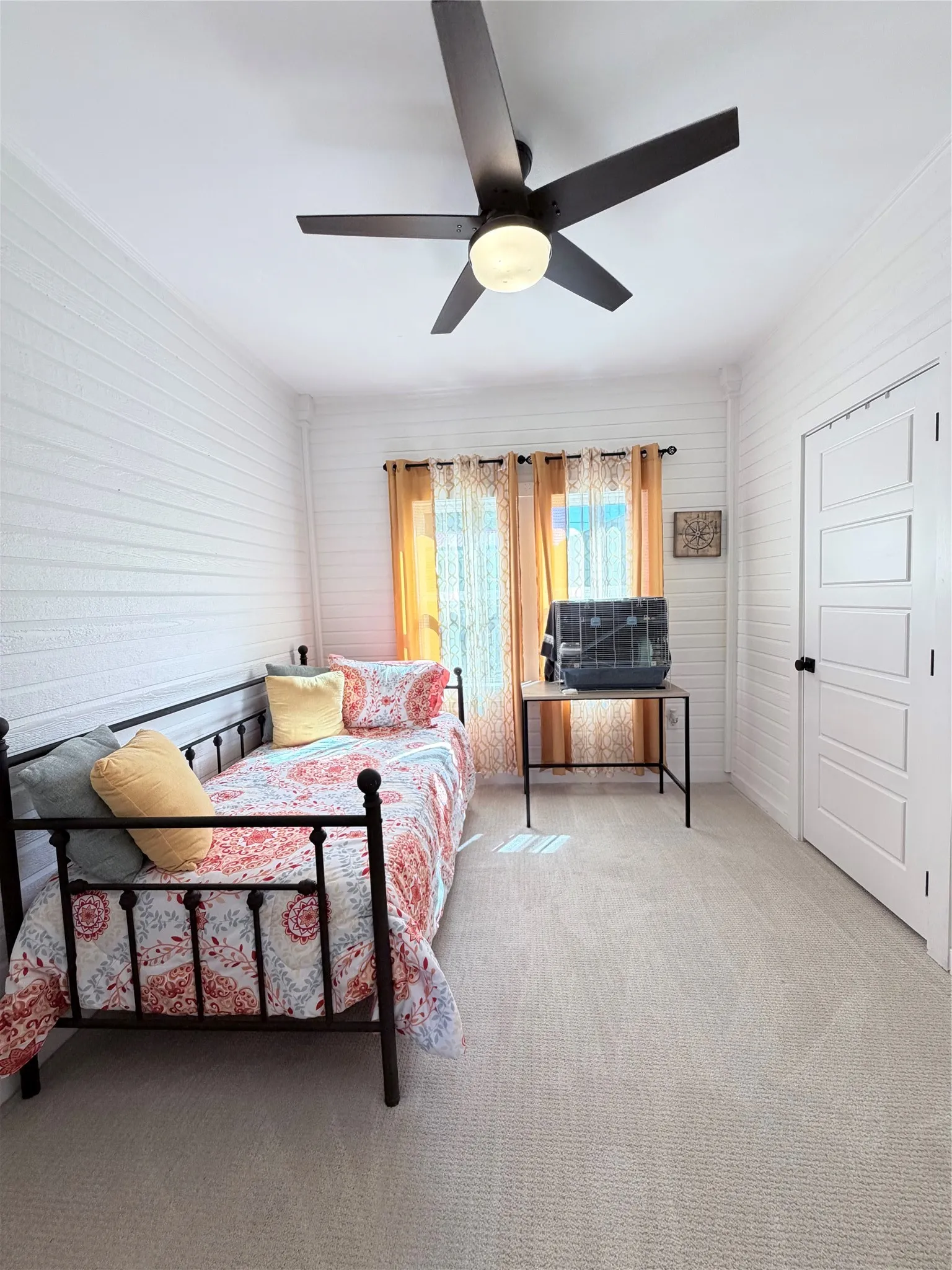 Horizontal shiplap walls, neutral wall-to-wall carpeting, multi-panel interior door with matte black hardware, and a contemporary ceiling fan with integrated lighting
