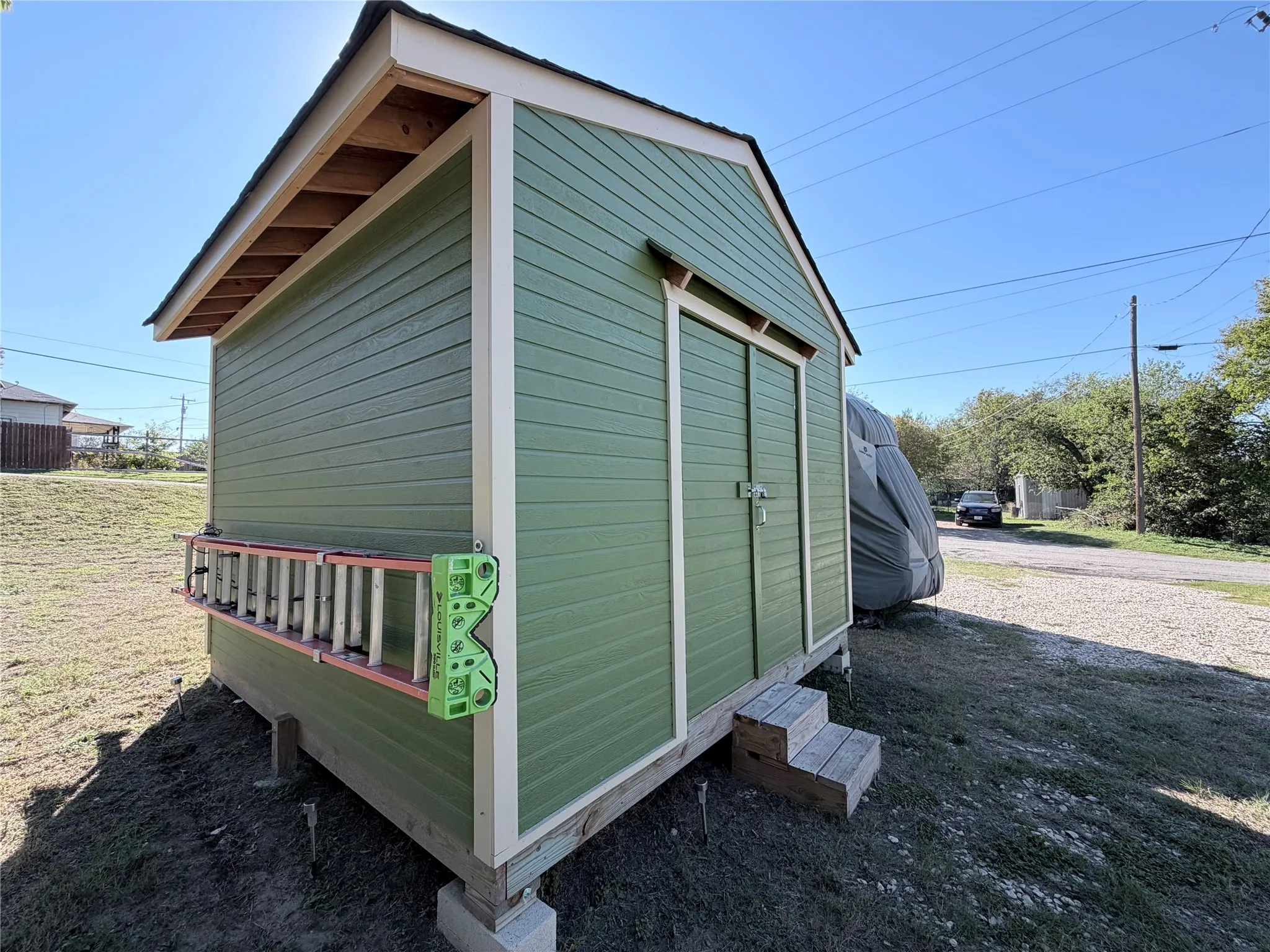 Green storage structure with lap siding, contrasting trim, double-door entry, and raised wood platform steps