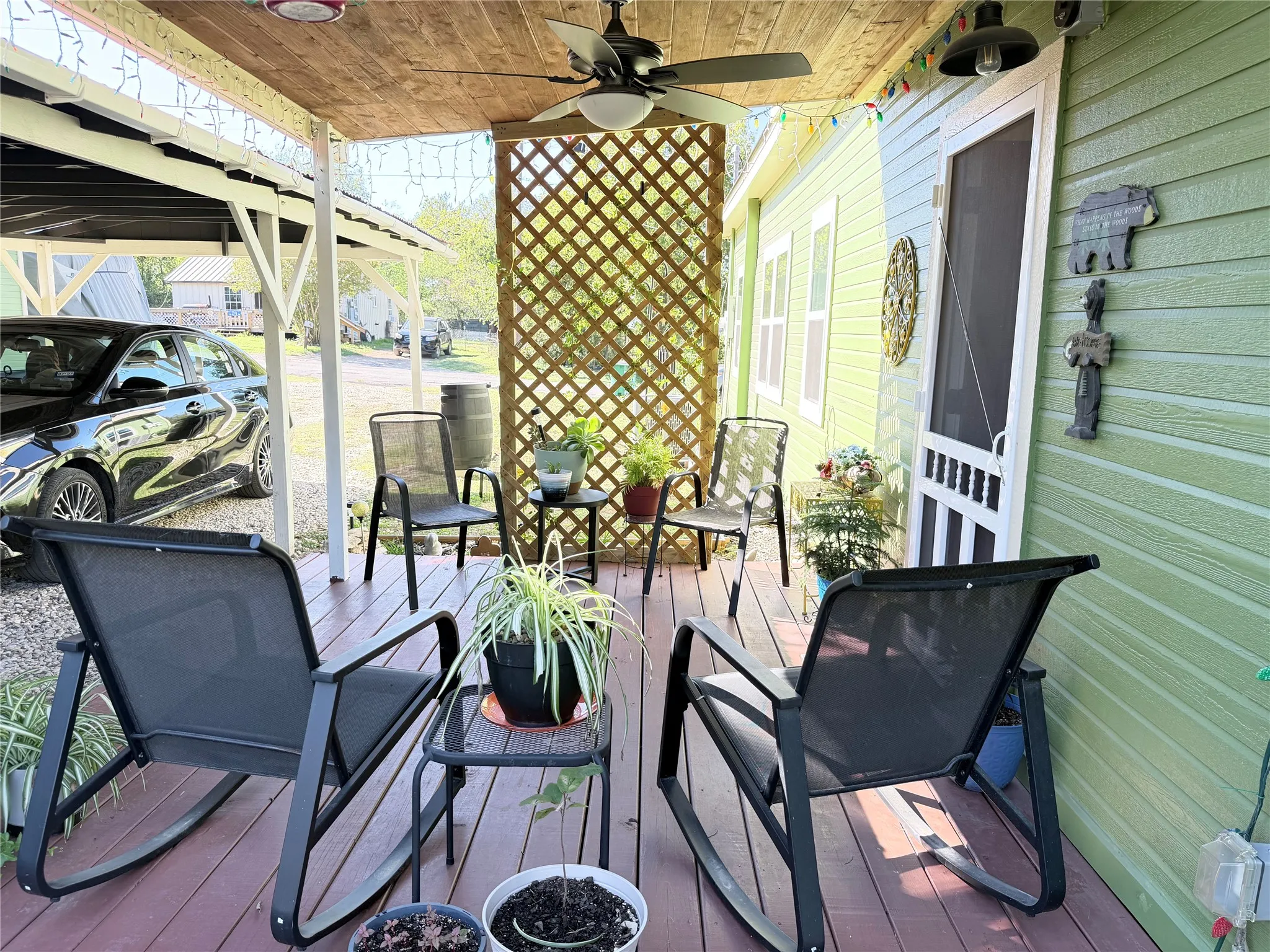 Covered side porch featuring wood-finish decking, a natural wood-paneled ceiling, a central ceiling fan, and decorative wood lattice screening