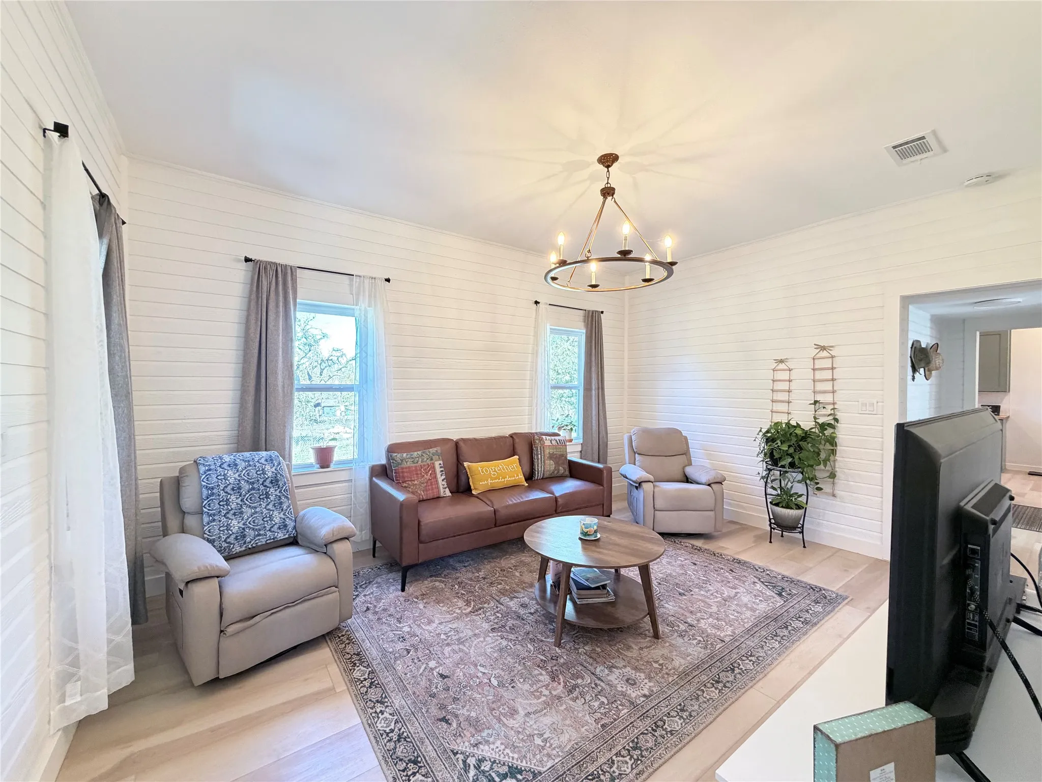 Living area featuring horizontal shiplap wall paneling, light wood-finish flooring, and a multi-arm metal chandelier