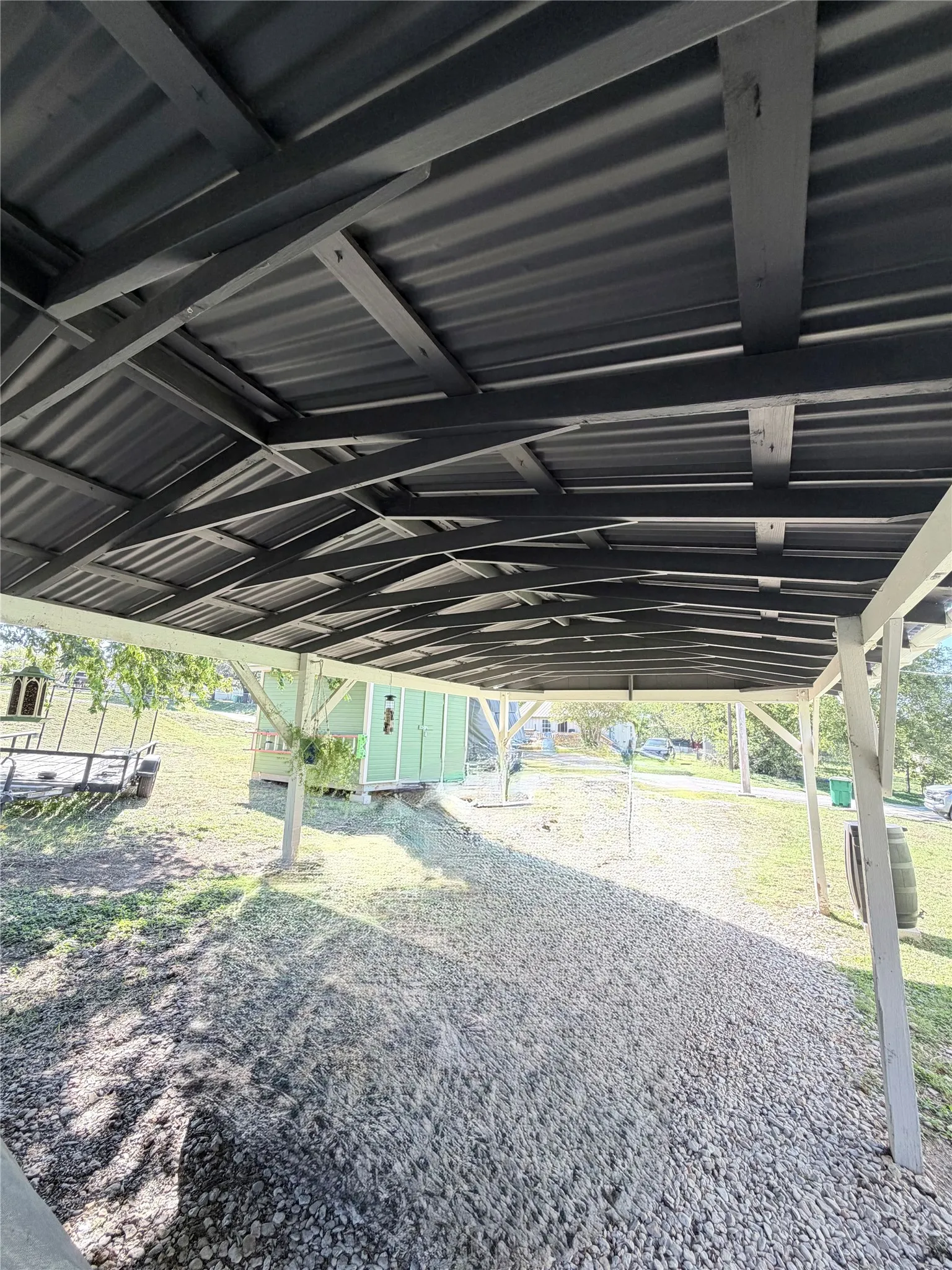 Covered carport featuring a metal roof, exposed structural beams, and a leveled gravel base