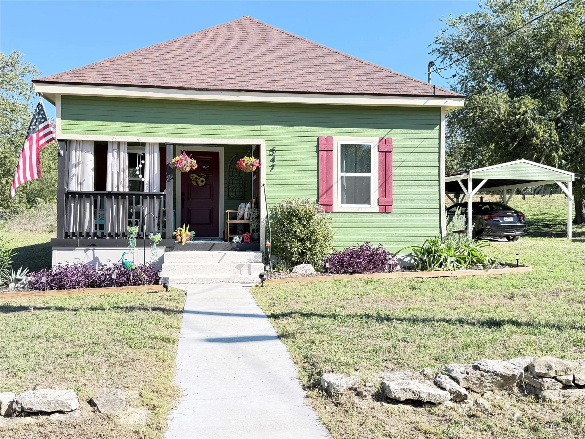 Single-story residence featuring horizontal lap siding, a covered front porch with railings, decorative window shutters, and a detached carport
