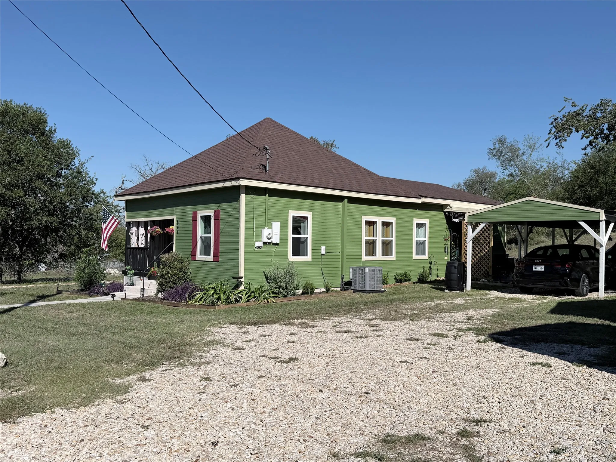 Single-story exterior with horizontal siding, hipped roofline, gravel driveway, and attached carport