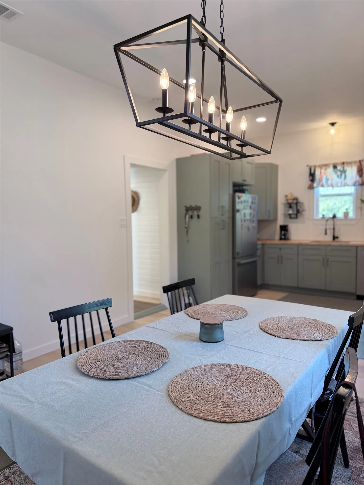 Geometric matte black lantern chandelier, sage green shaker-style cabinetry, and recessed lighting