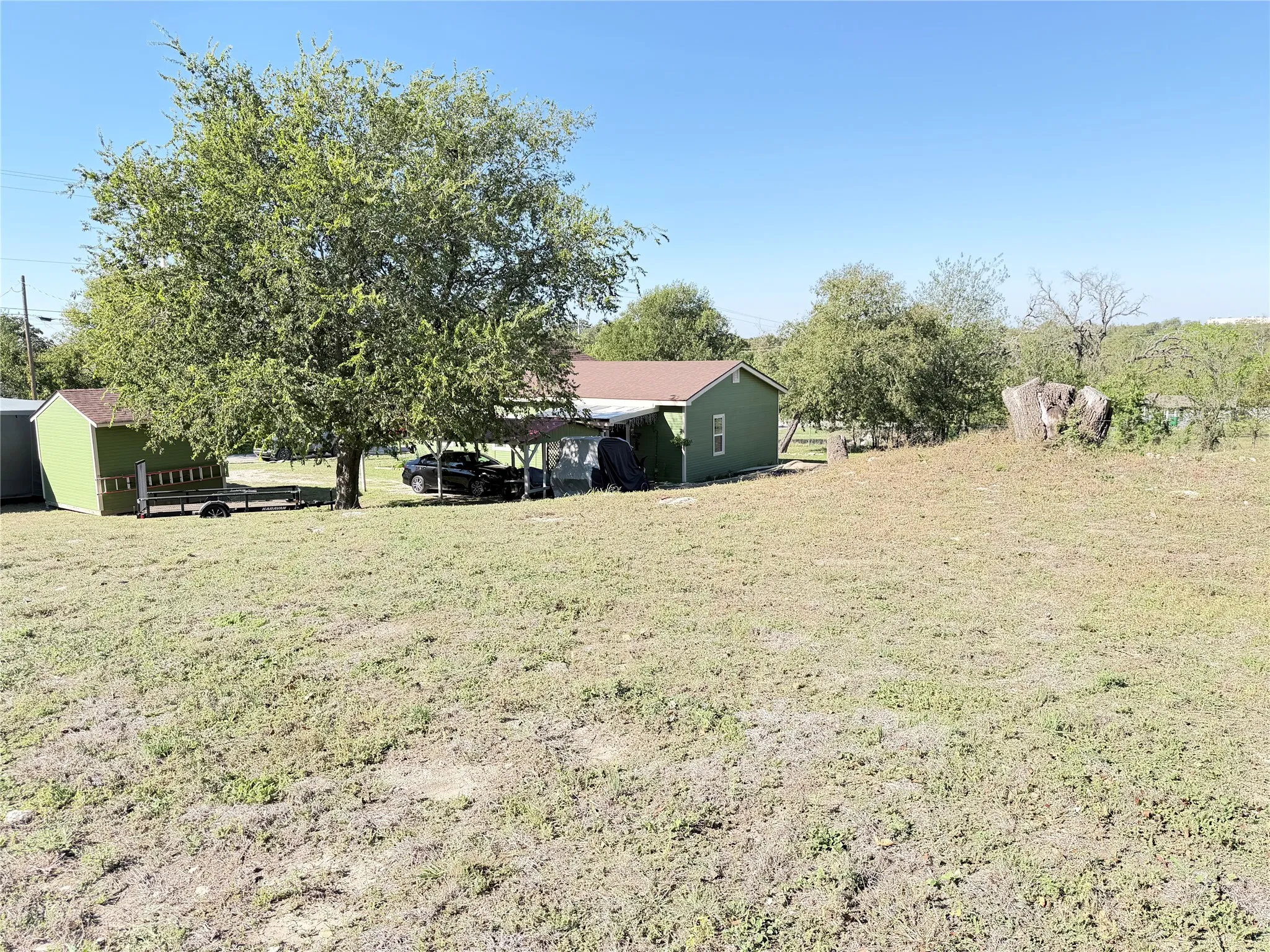 Expansive lot featuring mature trees, natural terrain, a detached storage structure, and a residence with an attached covered area