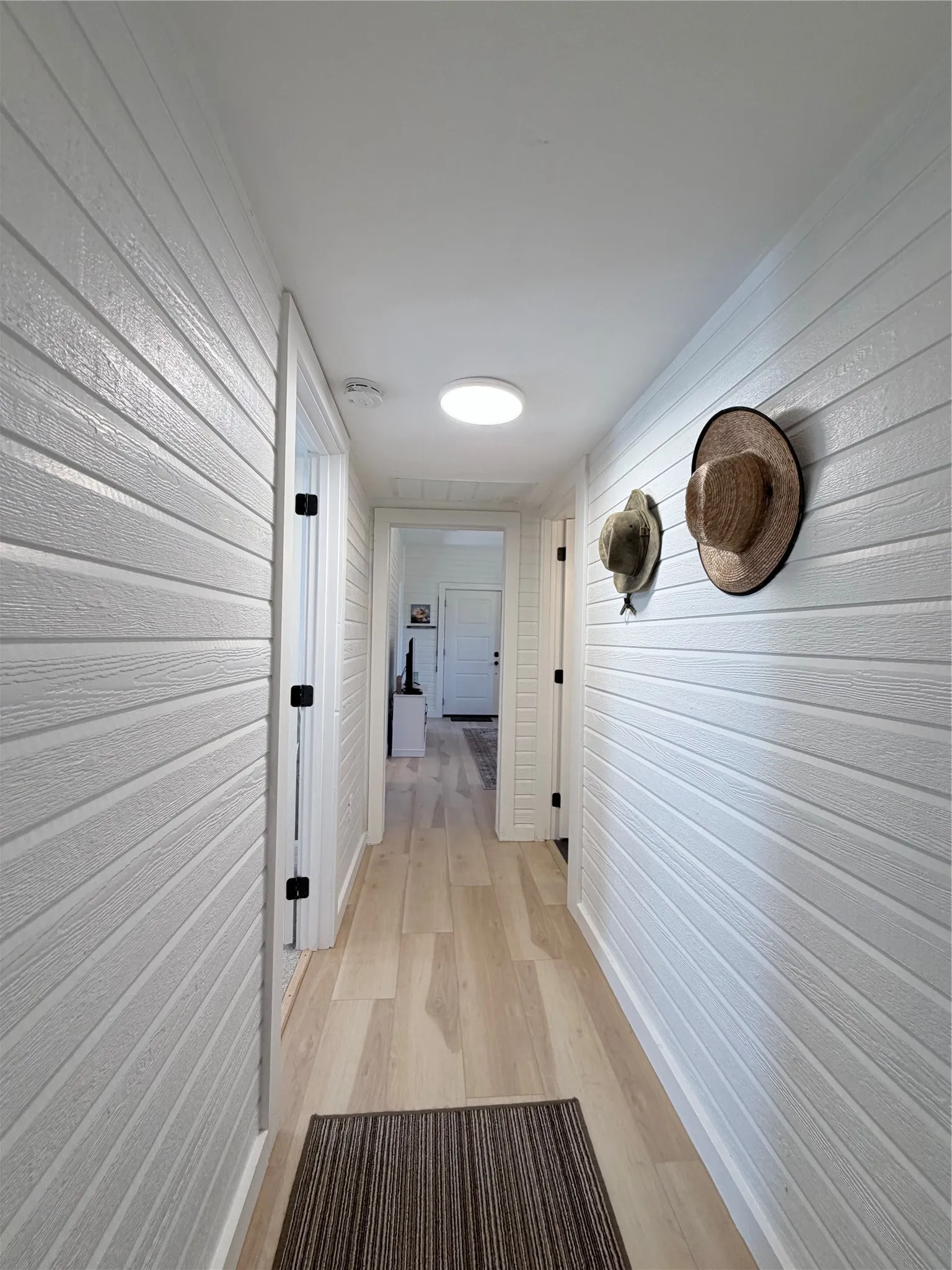 Hallway featuring horizontal white wood-finish plank wall paneling, light-tone wood-finish flooring, and minimalist ceiling-mounted lighting