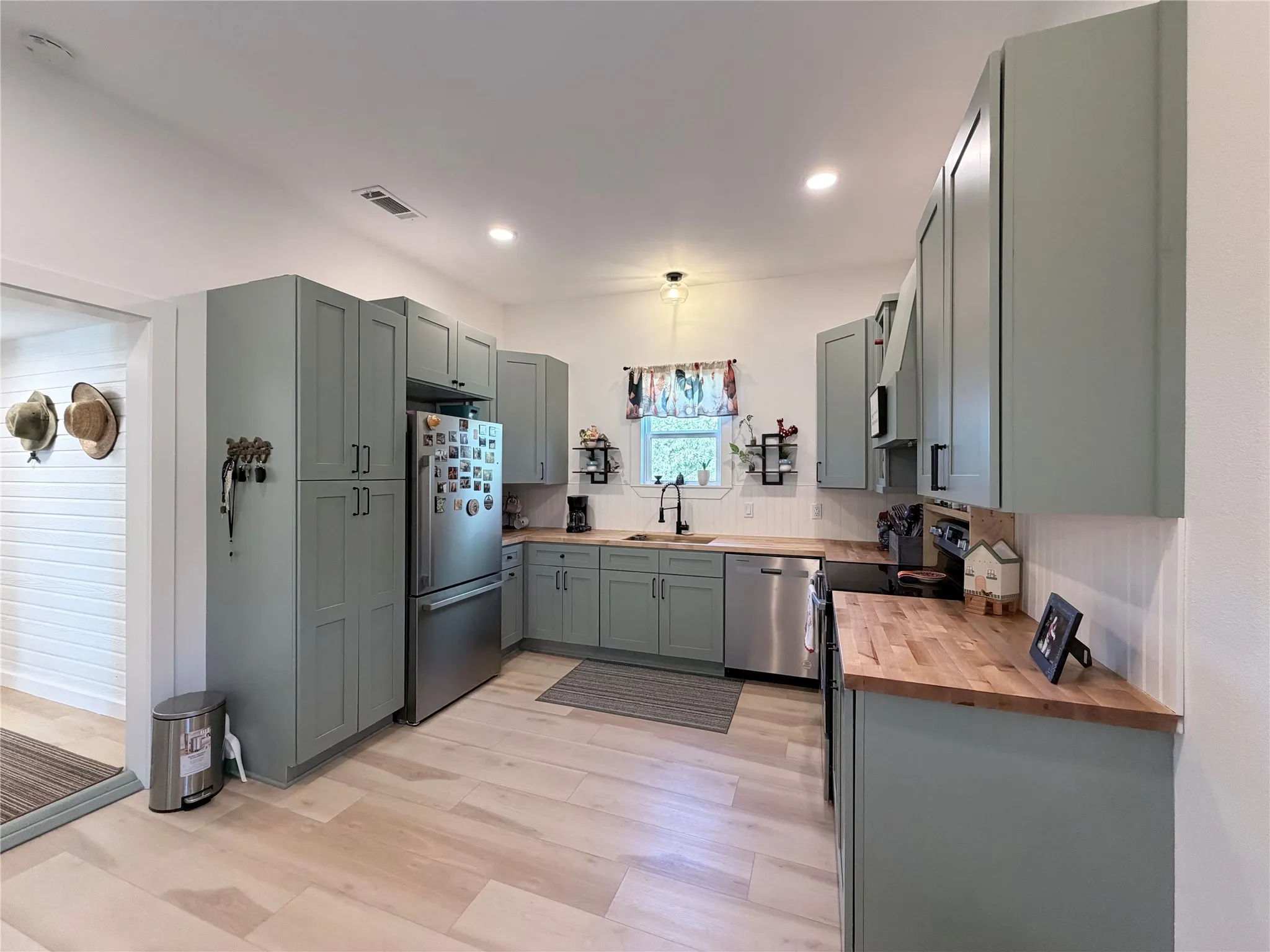 Kitchen featuring sage green cabinetry, butcher block countertops, wood-finish flooring, recessed lighting, and stainless steel appliances