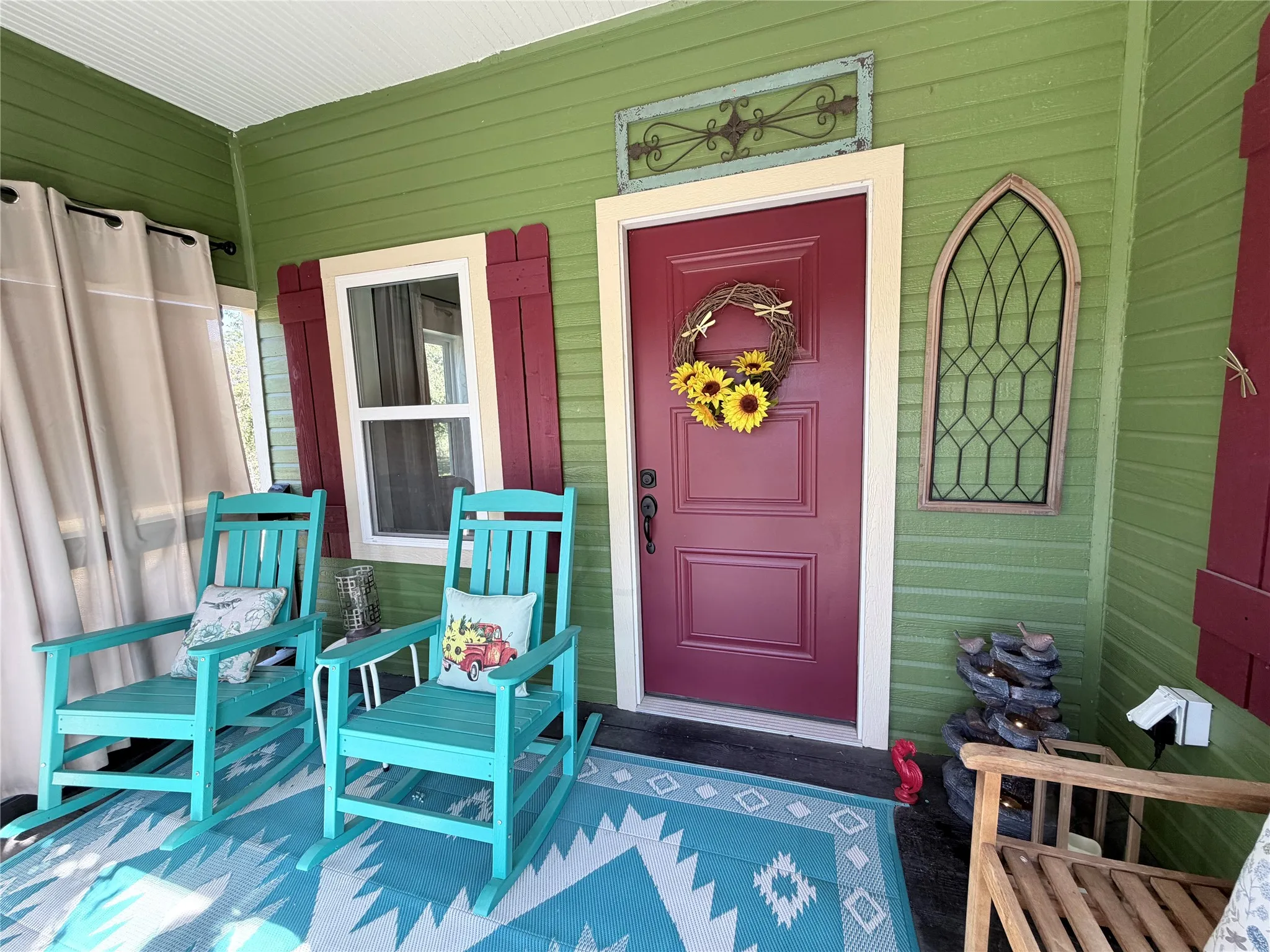 Covered porch featuring lap siding, paneled front door, window with shutter accents, and arched wall decor