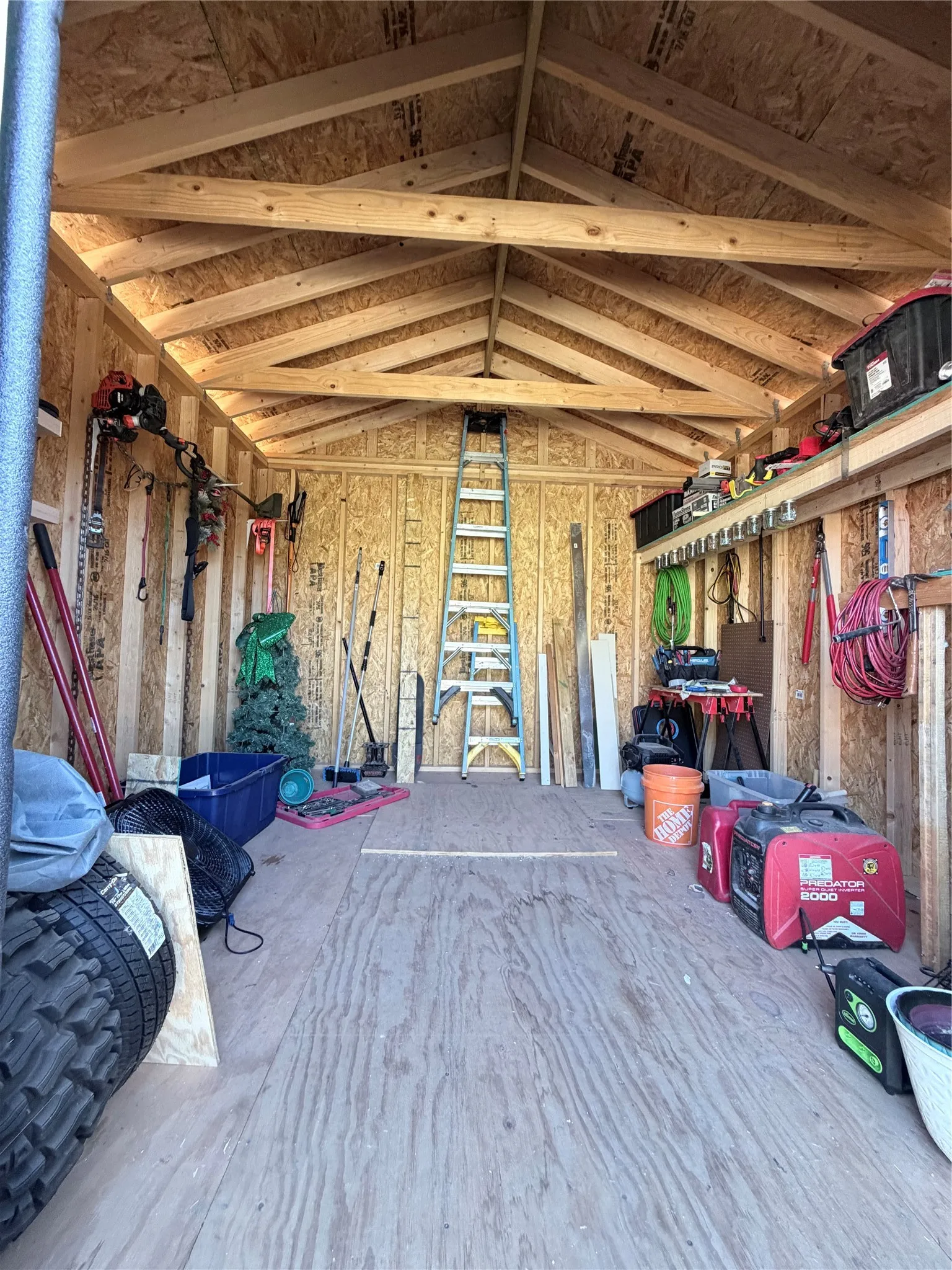 Storage structure featuring exposed wood framing, vaulted roof trusses, plywood flooring, and integrated wall-mounted shelving