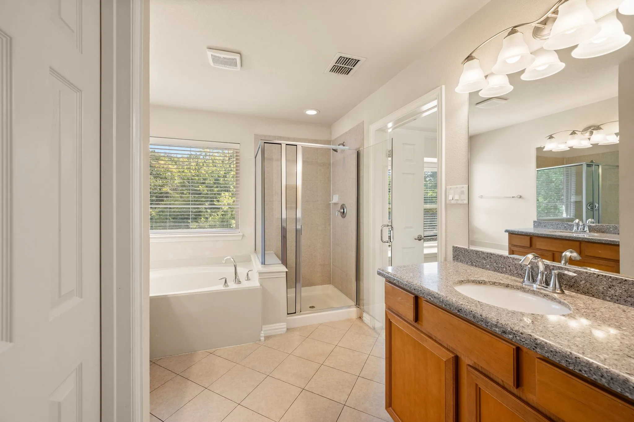 Bathroom featuring a vanity with stone-finish countertop, undermount sink, tiled walk-in shower with glass enclosure, deep soaking tub, and tile flooring
