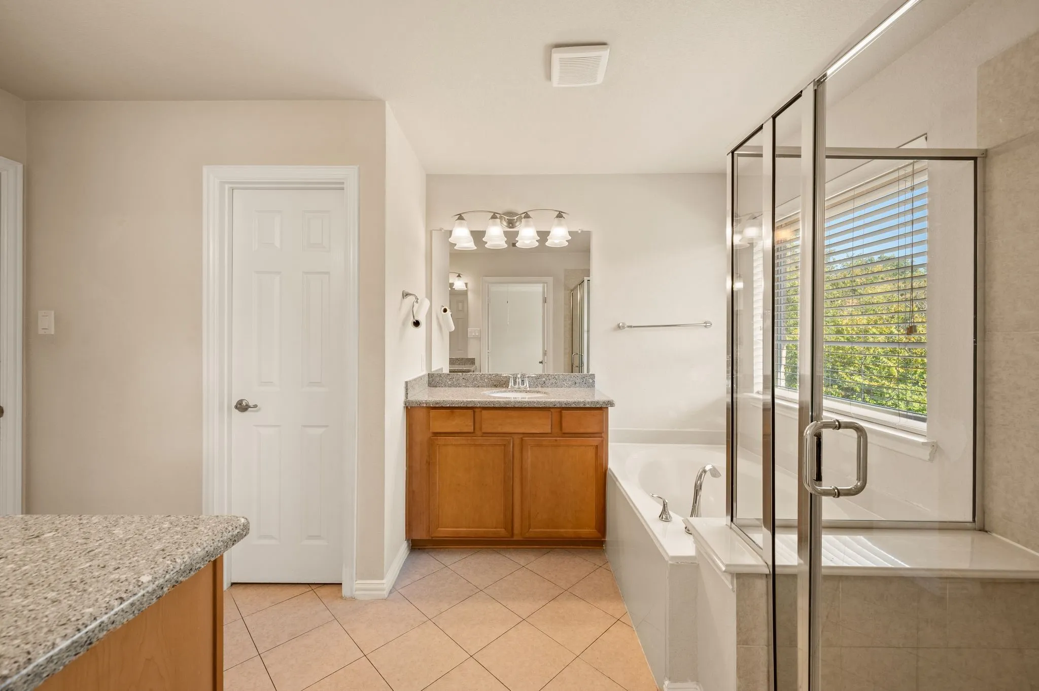 Bathroom featuring wood-finish cabinetry, stone-composite countertop with an integrated sink, glass-enclosed shower, soaking tub, and ceramic tile flooring