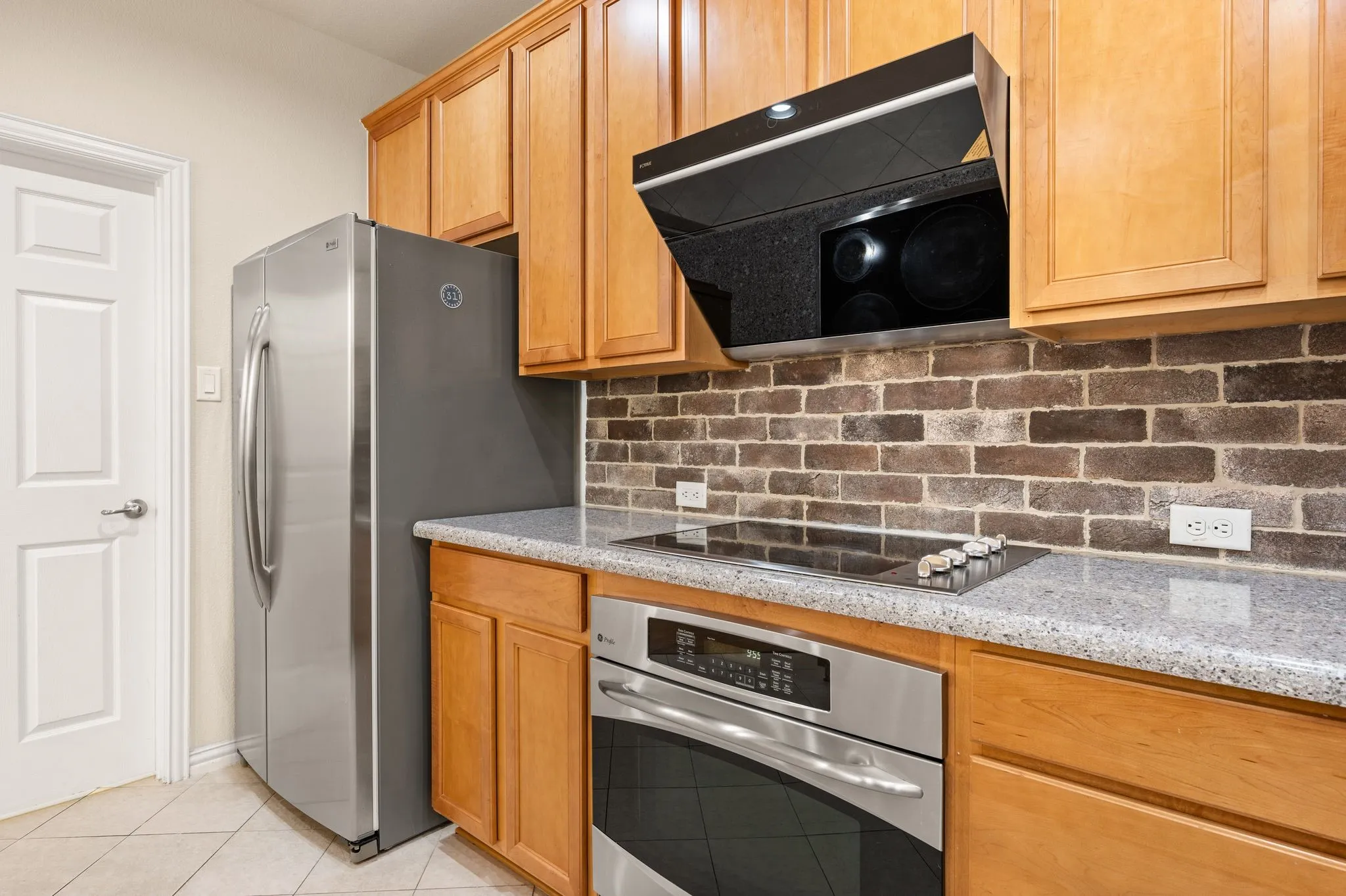 Kitchen featuring wood cabinetry, stone-finish countertops, stainless steel appliances, and a textured brick backsplash