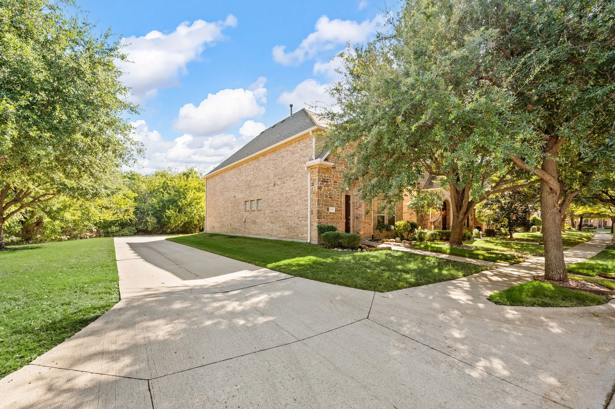 Brick exterior featuring a concrete driveway and mature trees on a landscaped lot