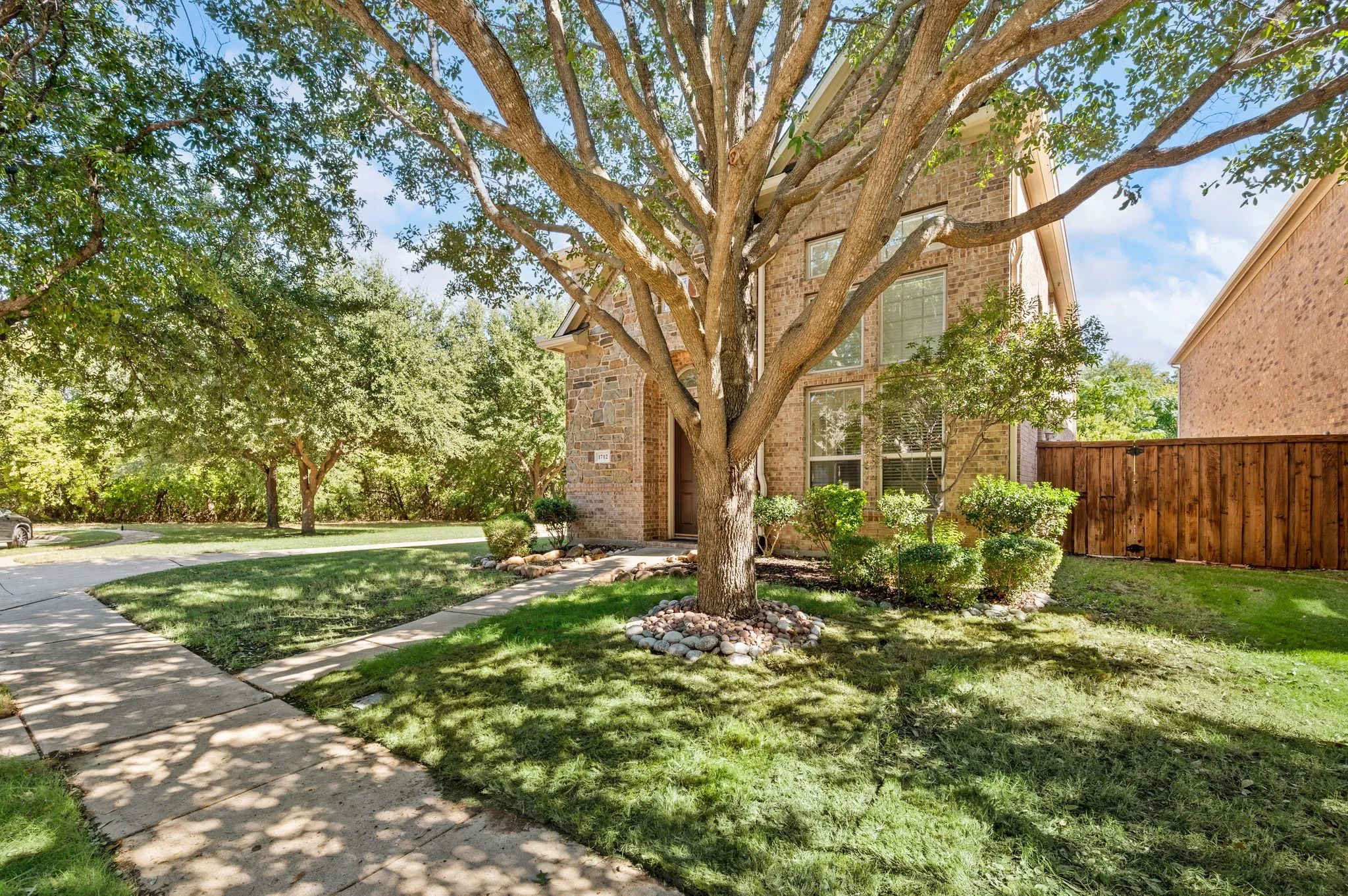 Brick exterior featuring multi-story window configurations, concrete paved walkways, manicured landscaping, and mature trees