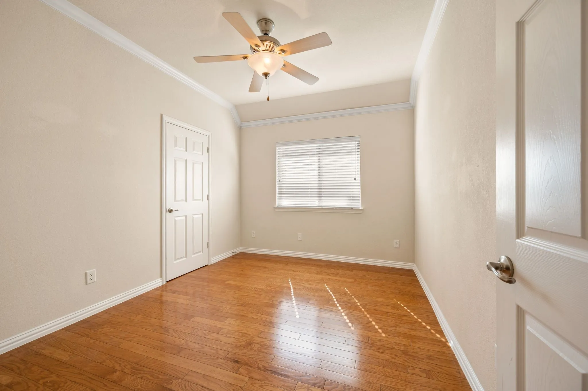 Room featuring wood-finish flooring, vaulted ceilings, crown molding, a central ceiling fan with integrated lighting, and a window with horizontal blinds