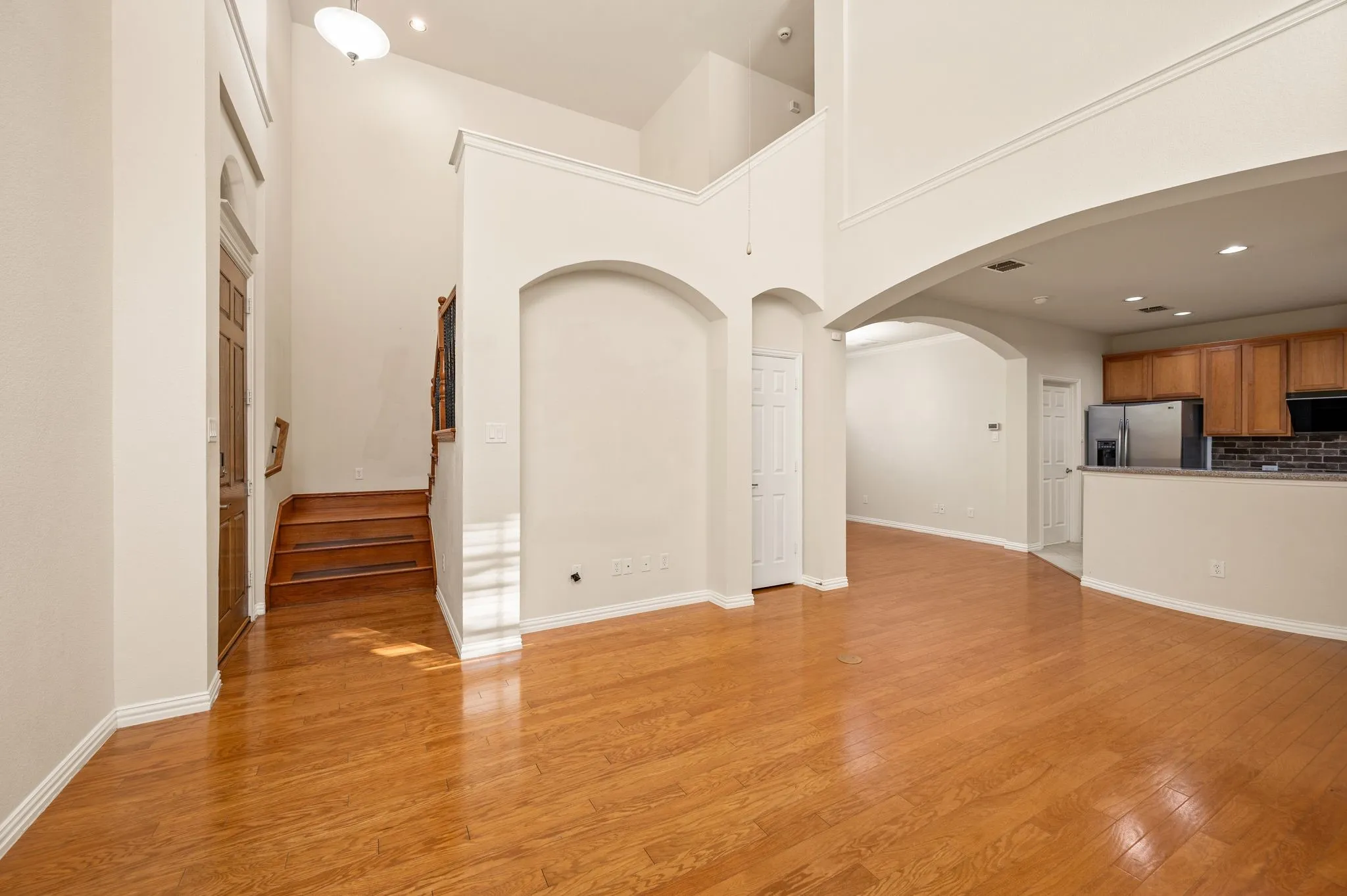 High-ceiling interior featuring wood-finish flooring, architectural arched wall niches, recessed lighting, and a breakfast bar
