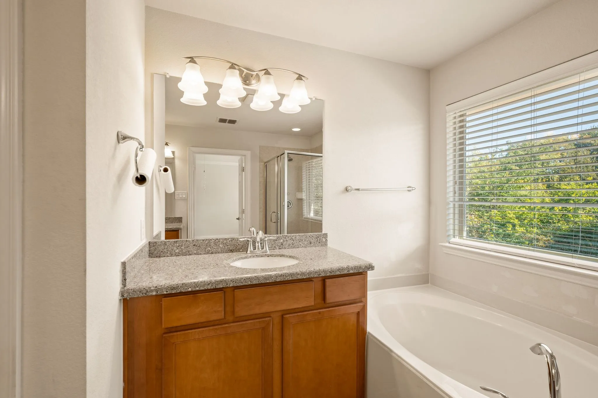 Bathroom vanity featuring a stone-composite countertop, undermount sink, multi-bulb light fixture, and deep-toned wood cabinetry, accompanied by a built-in soaking tub