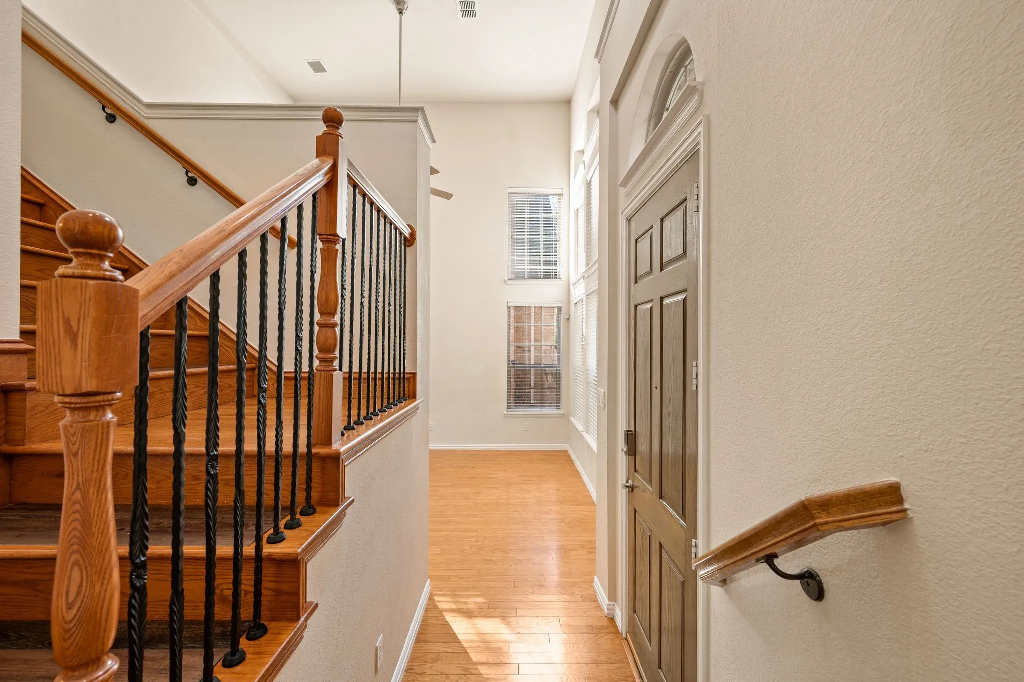 Entryway featuring high ceilings, wood-finish flooring, staircase with wood handrails and metal balusters, and multi-pane windows with arched transom detail