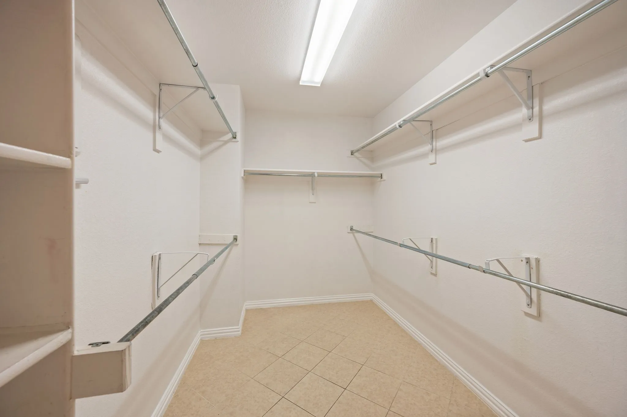 Walk-in closet featuring multi-level metal hanging rods, integrated wall shelving, linear ceiling lighting, and tiled flooring