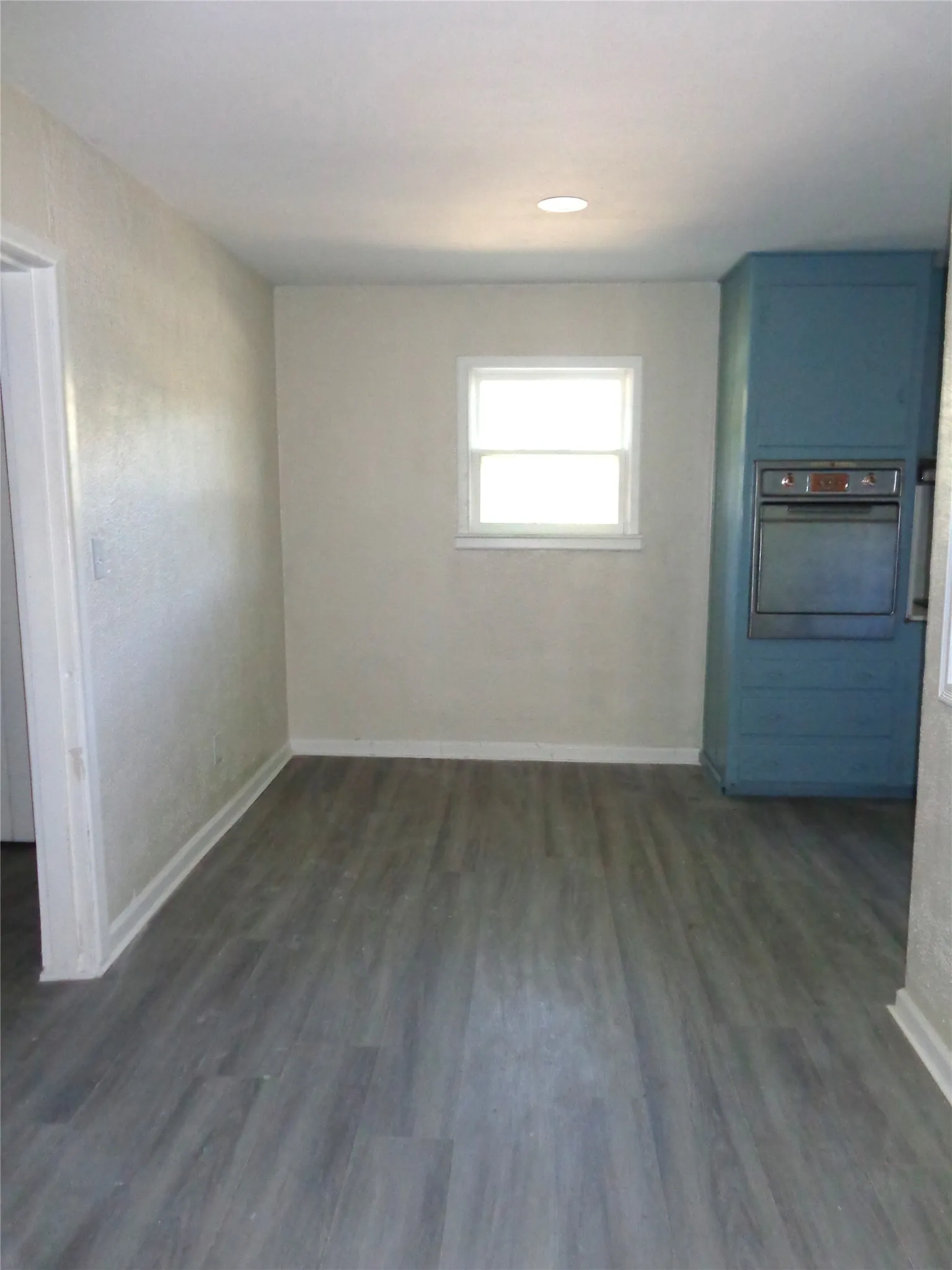 Neutral-toned walls, wood-finish flooring, recessed lighting, double-hung window, and integrated blue cabinetry featuring a built-in oven