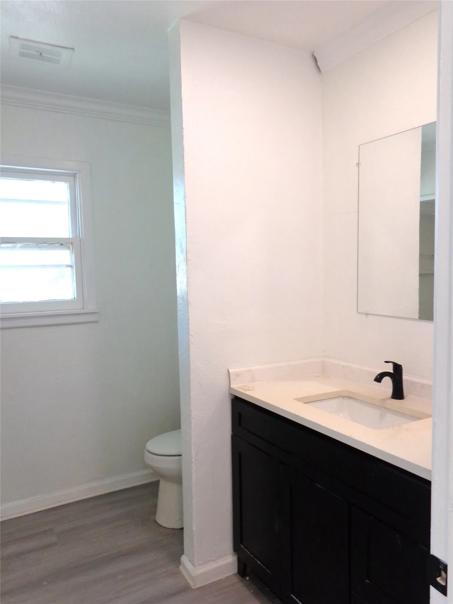Bathroom featuring a vanity with a dark-toned cabinet, light-toned countertop, rectangular undermount sink, and matte black faucet, finished with wood-finish flooring and a rectangular wall mirror