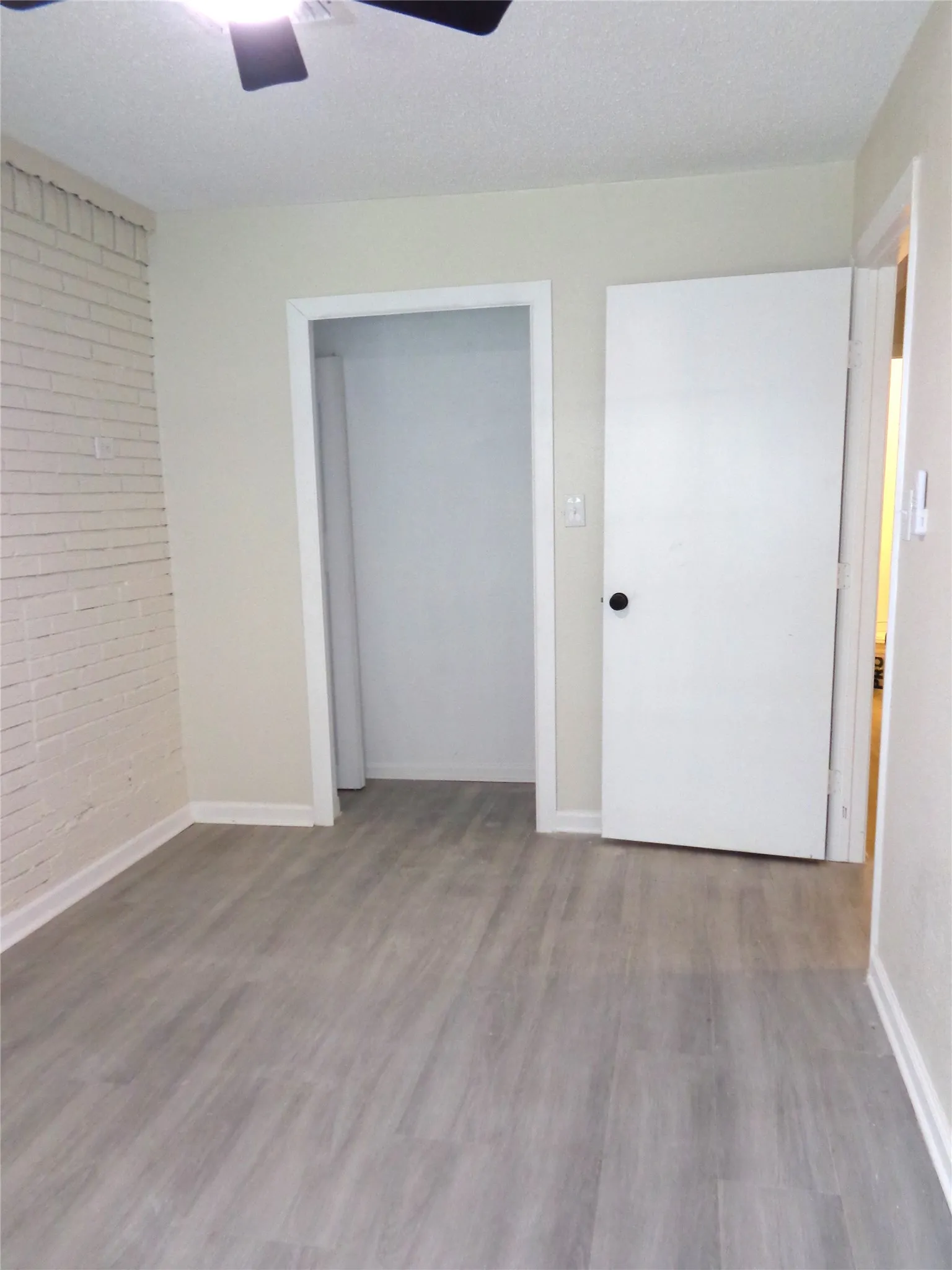 This could be a 4th Bedroom, Nursery, or Office. Interior space featuring wood-finish flooring, a painted brick accent wall, multi-pane windows, and a modern ceiling fan with integrated lighting