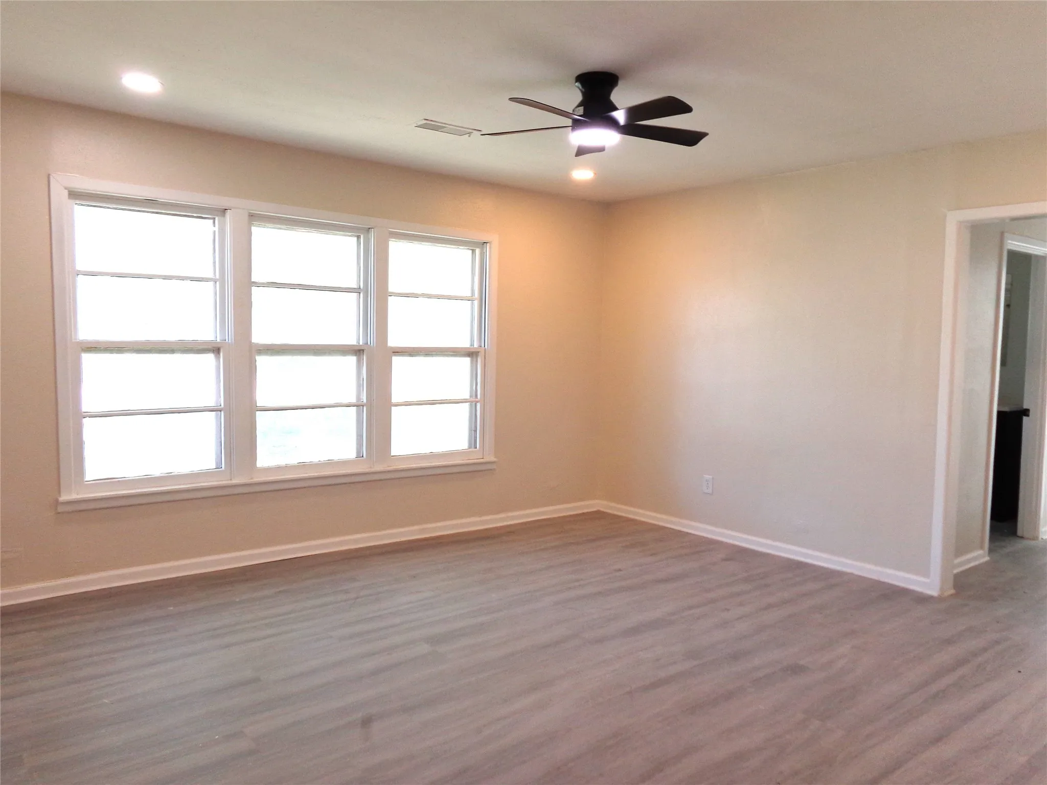 Neutral wall-toned room featuring wood-finish flooring, multi-pane windows, recessed ceiling lighting, and a central ceiling fan with an integrated light fixture