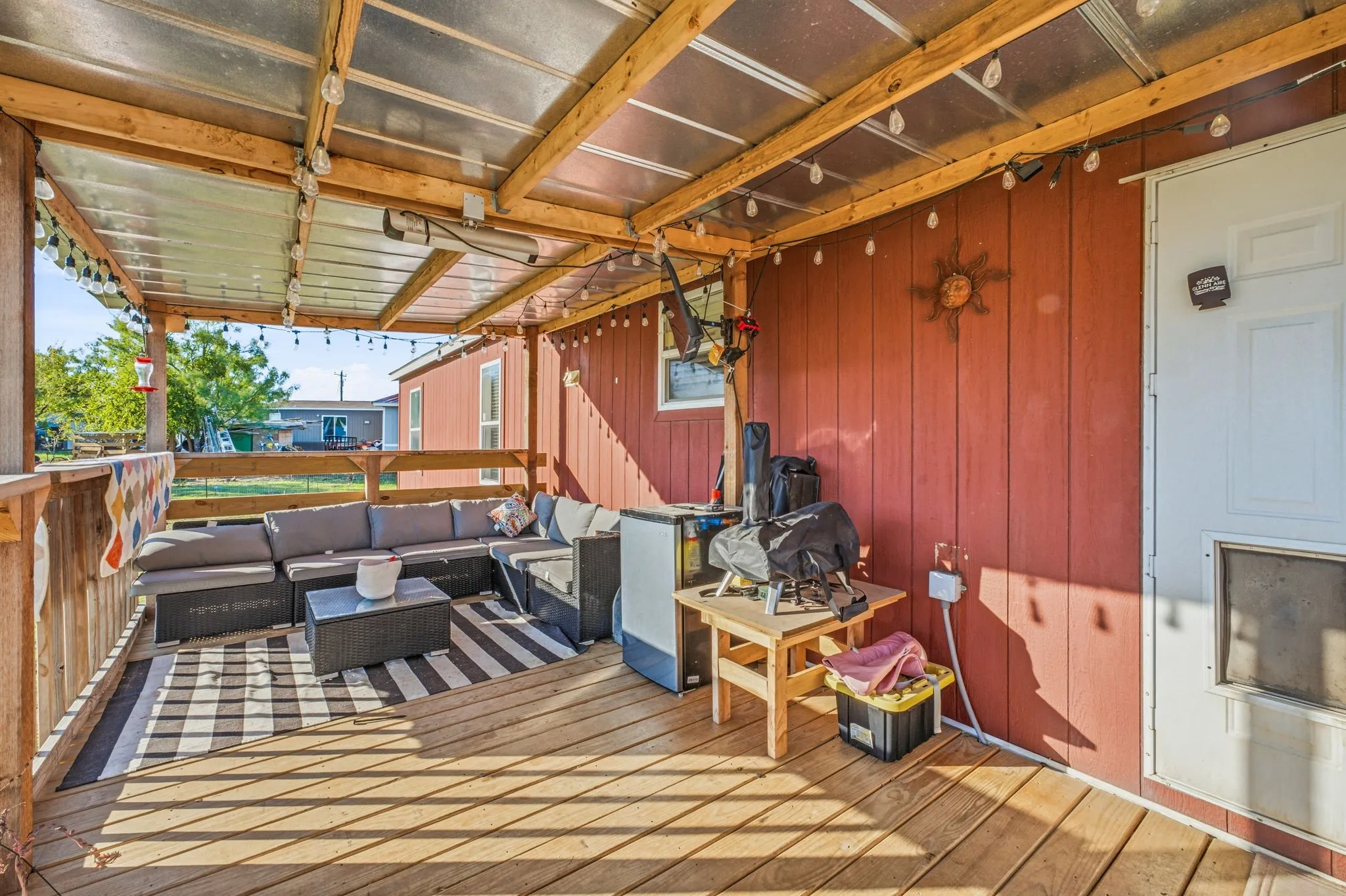 Covered outdoor deck featuring wood-plank flooring, a timber-framed structure with a translucent roof, wooden railings, and vertical exterior siding