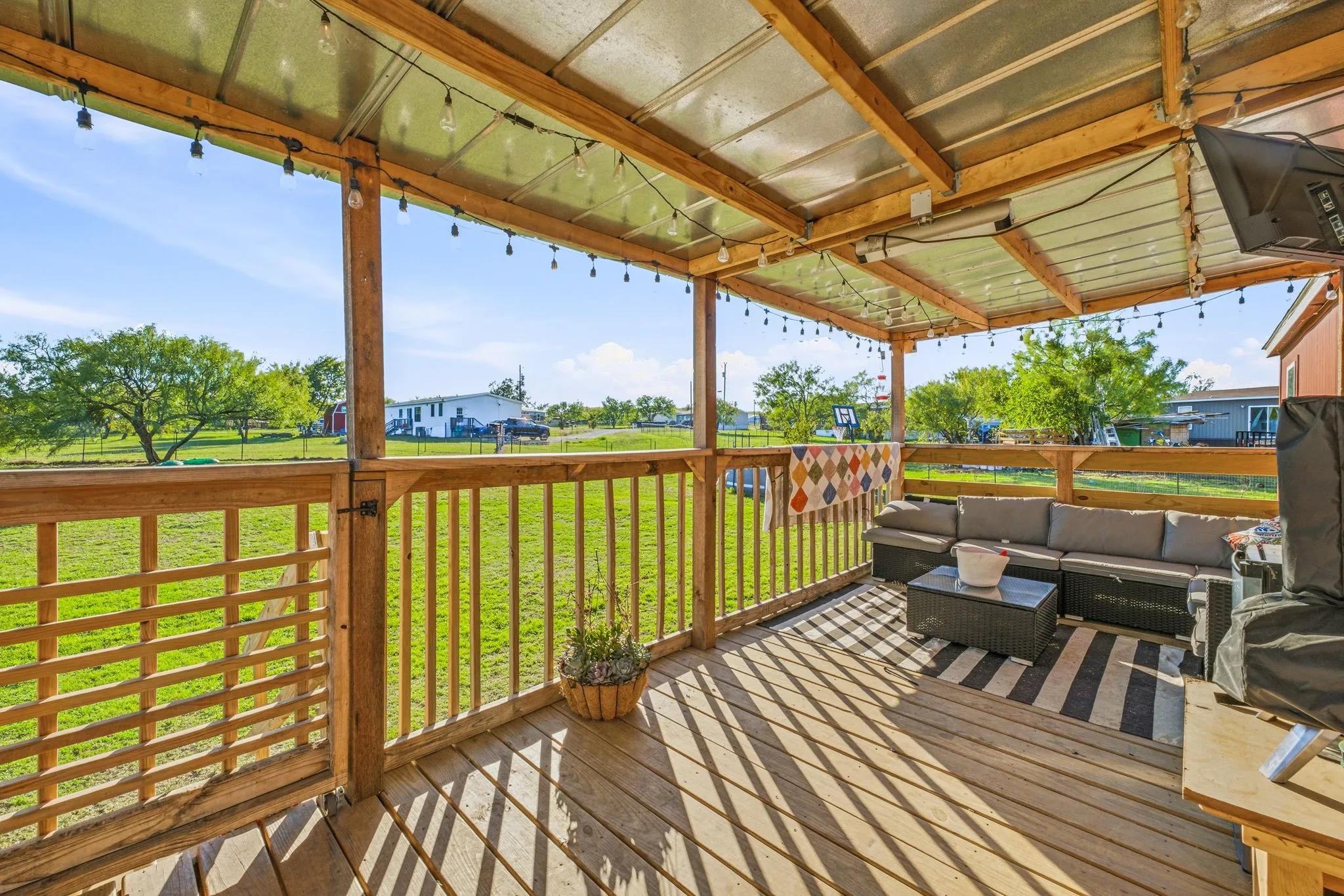 Covered wooden deck featuring a metal roof, wood-slat railing, and built-in string lighting