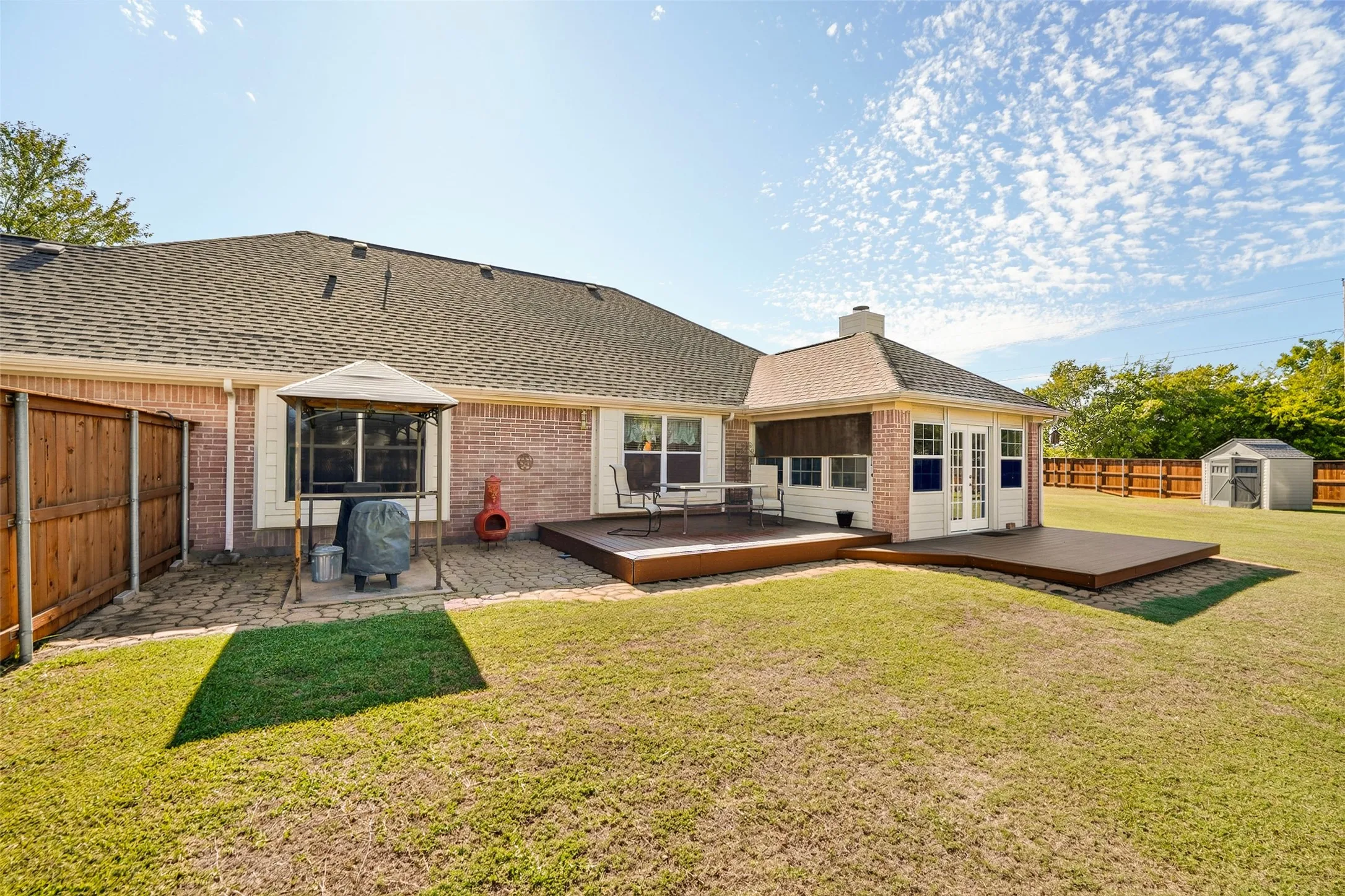 Sunroom opens up to a multi-level TREX deck, paved patio area with BBQ canopy, wood fencing, and a detached storage shed.