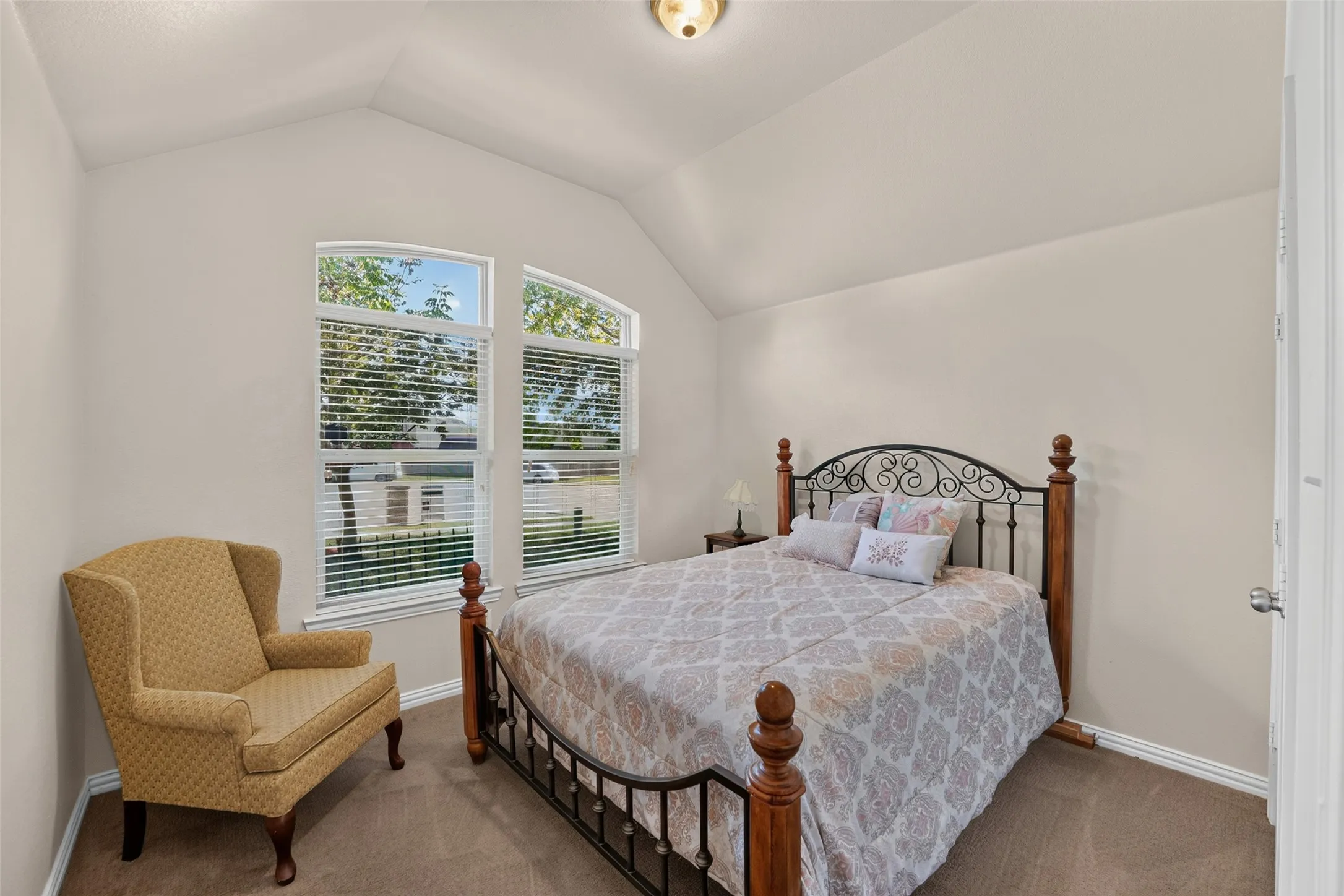 Sec. bedroom in front of home with a vaulted ceiling featuring a central flush-mount light fixture and dual arched windows with blinds.
