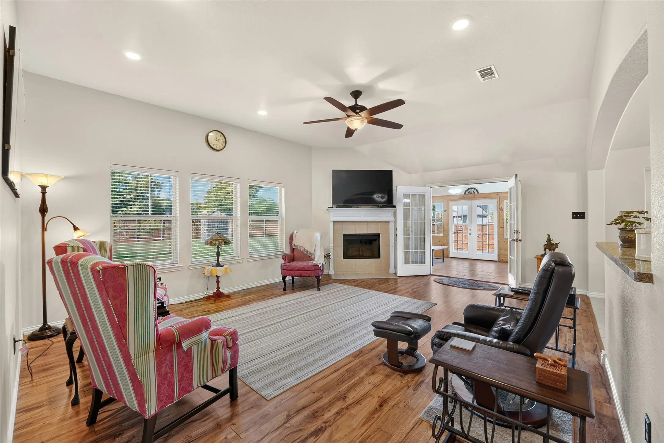 Spacious living room with vaulted ceilings, abundant natural light, a cozy fireplace, and access to the sunroom via double doors.